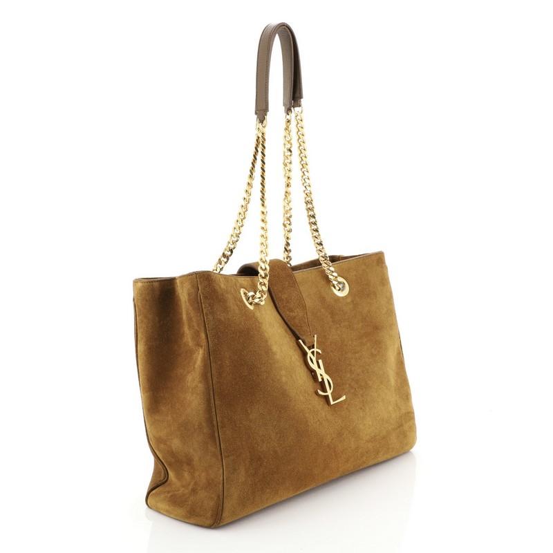 This Saint Laurent Classic Monogram Shopper Suede Large, crafted from brown suede, features dual gourmette chain straps with leather pads, YSL logo, and gold-tone hardware. It opens to a black fabric interior with a center zip compartment and side