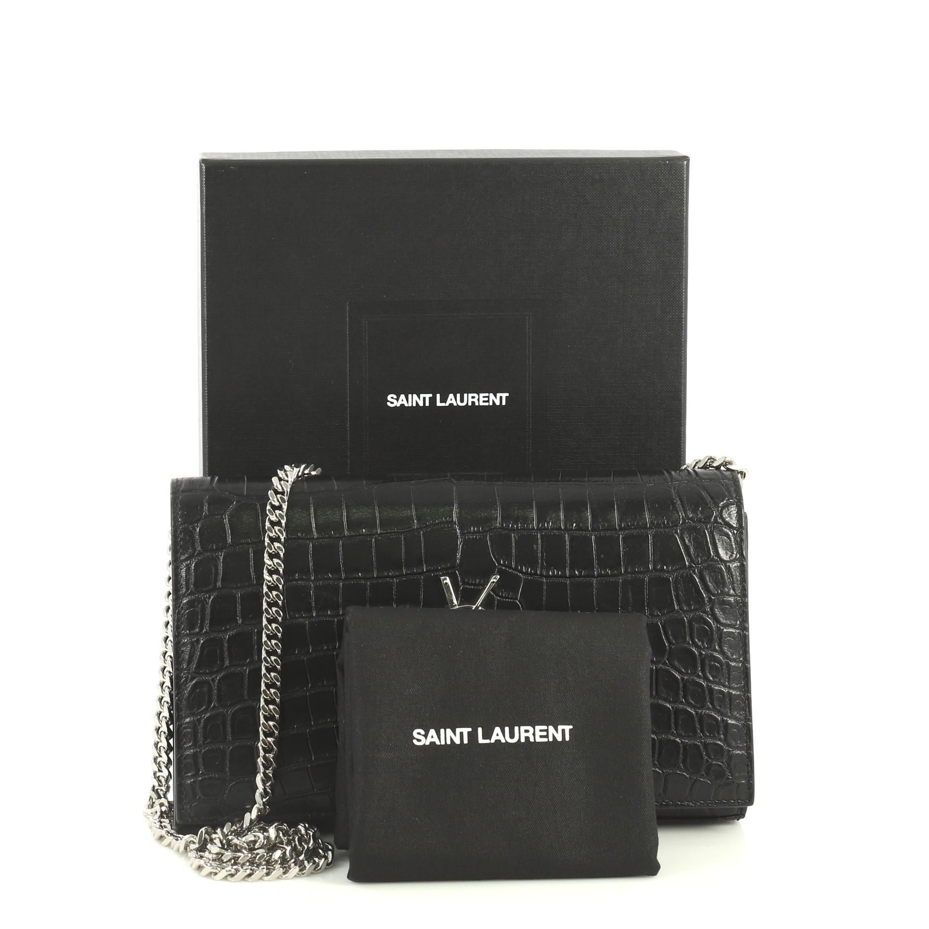 This Saint Laurent Classic Monogram Wallet on Chain Crocodile Embossed Leather, crafted from black crocodile embossed leather, features chain link strap, YSL monogram logo at the front, and silver-tone hardware. Its magnetic snap closure opens to a