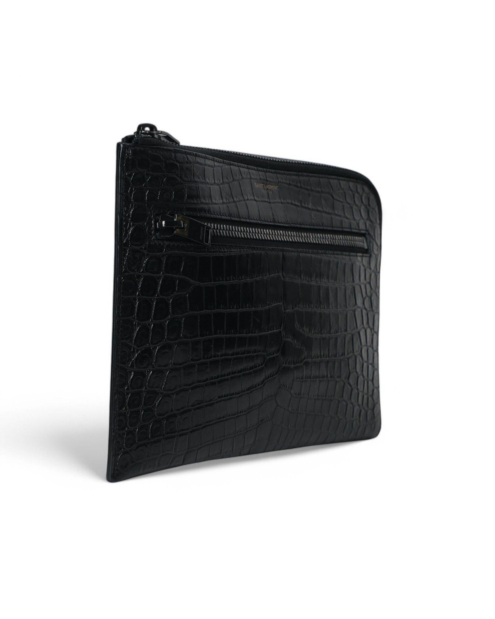 Clutch firmata Saint Laurent, misura small, realizzata in pelle lucida, hardware neri. Dotata di una chiusura semicircolare a zip, internamente rivestita in tessuto tono su tono con comode tasche, capiente per l’essenziale. Presenta una comoda tasca