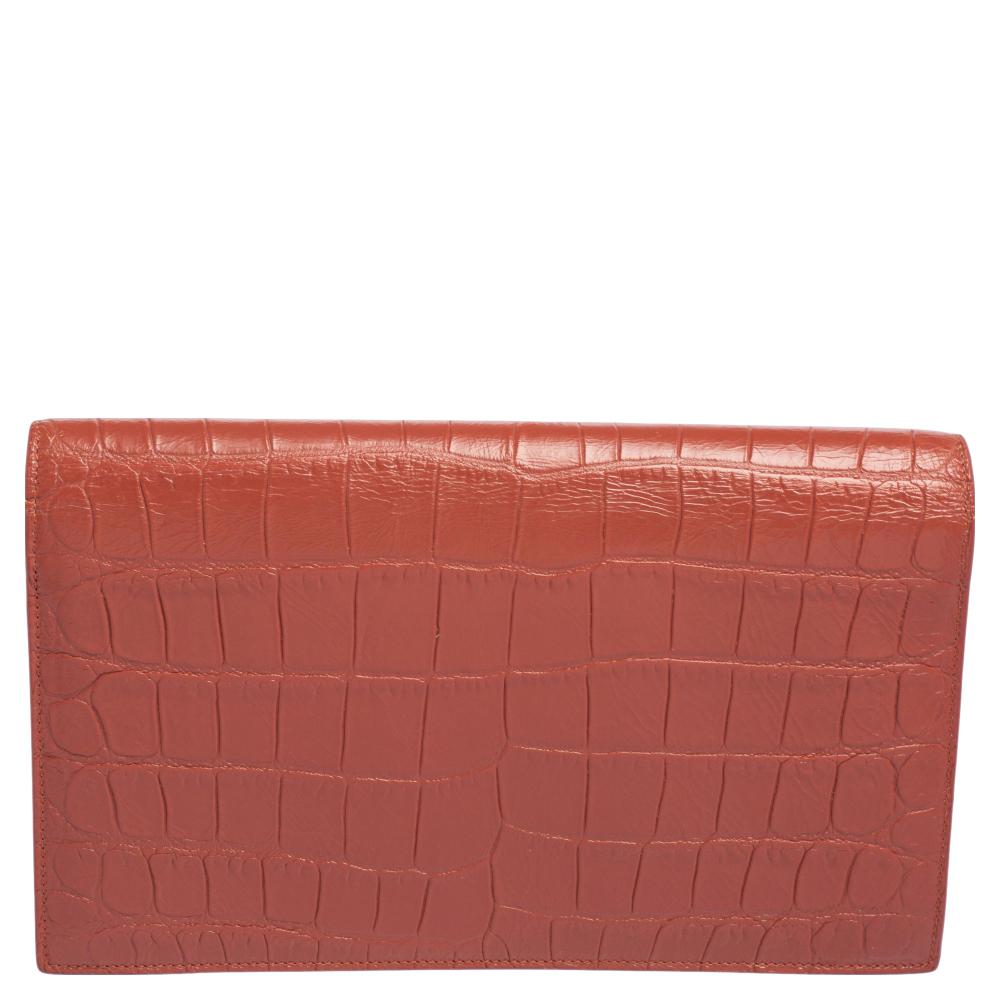 A classic and chic style with a glamorous look to it, this Saint Laurent clutch will take a special place in your collection for years to come. Crafted in brown croc-embossed leather and accented with silver-tone YSL monogram detail at the front