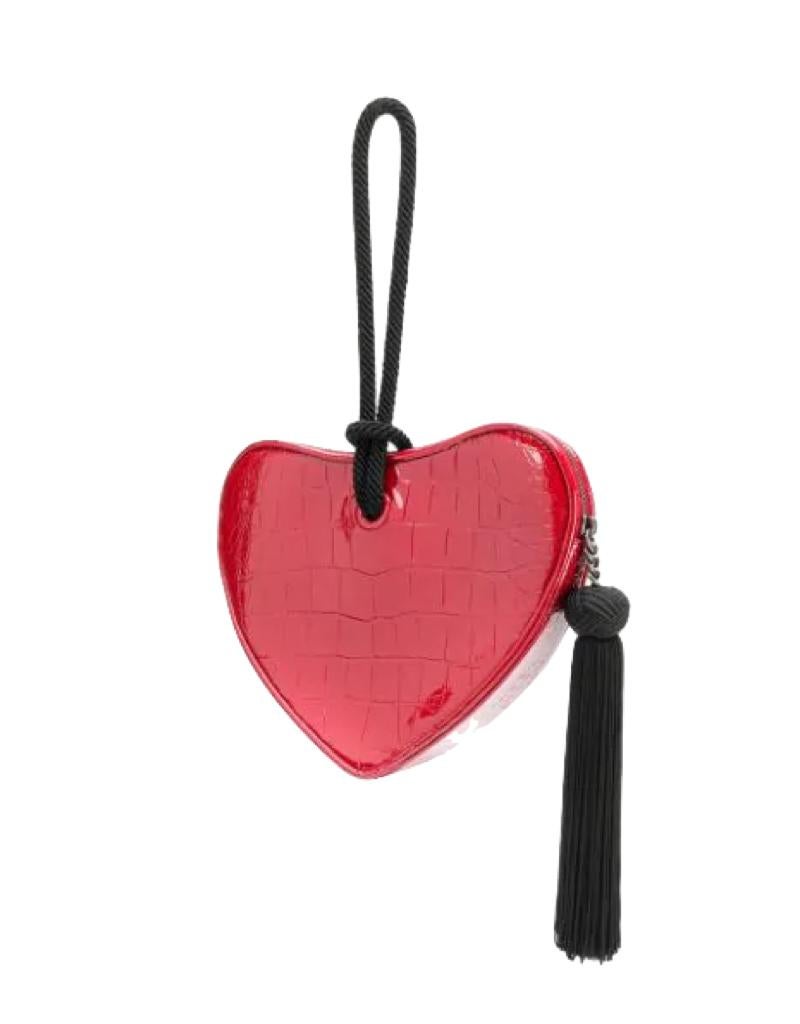 This clutch is made of embossed red leather in the shape of a heart. Sac coeur is French for heart bag. The handbag features an aged silver tone YSL logo, a black rope wristlet handle, and a black tassel zipper pull. The top zipper opens to a