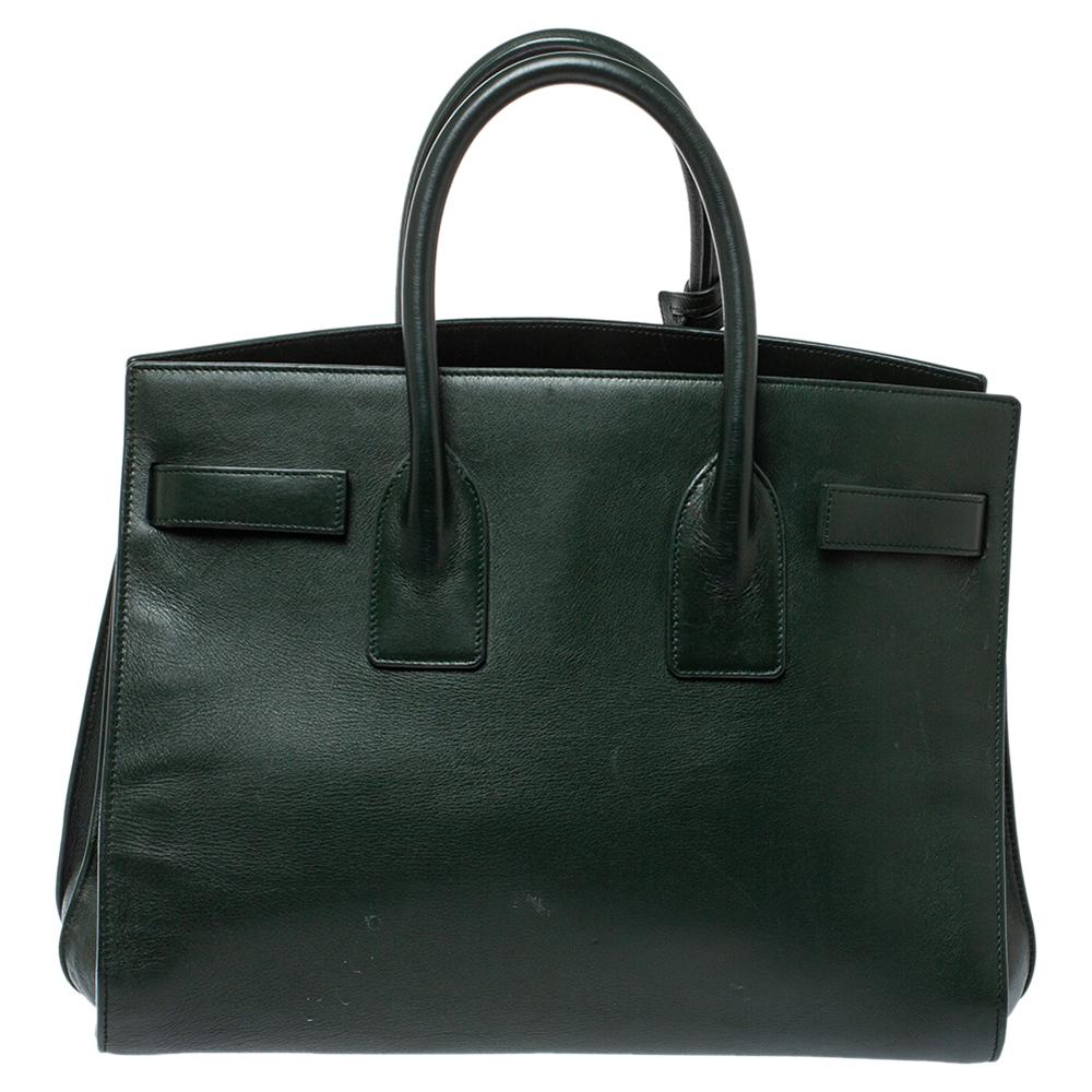 This Sac de Jour tote by Saint Laurent has a structure that simply spells sophistication. Crafted from dark green leather, the bag is held by double top handles. The tote comes with a suede-lined interior with enough space to store your necessities