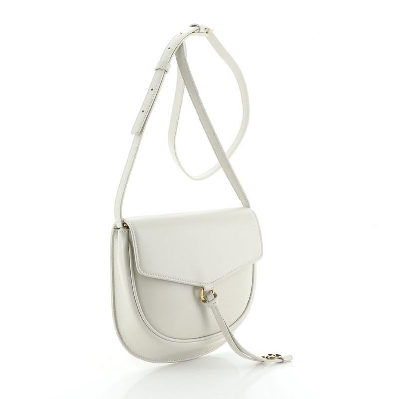 This Saint Laurent Datcha Crossbody Bag Leather Small, crafted in white leather, features an adjustable strap, saddle silhouette, YSL charm and gold-tone hardware. Its magnetic closure opens to a black leather interior with slip pockets. 

Estimated