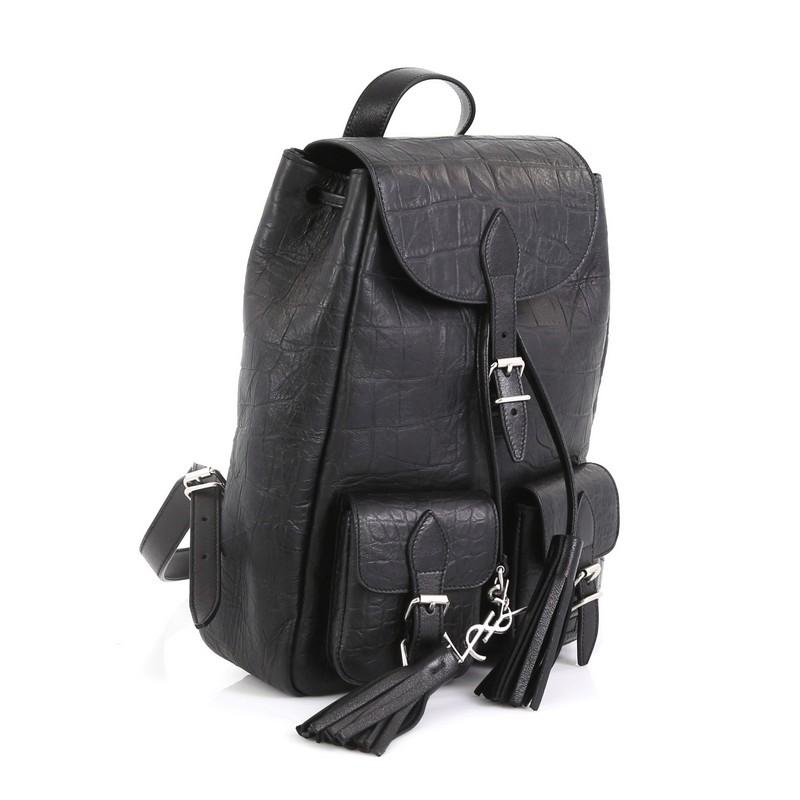 This Saint Laurent Festival Backpack Crocodile Embossed Leather Small, crafted from black leather, features adjustable leather shoulder straps, top handle, two exterior front pockets with buckles, top flap with buckle closure, and silver-tone