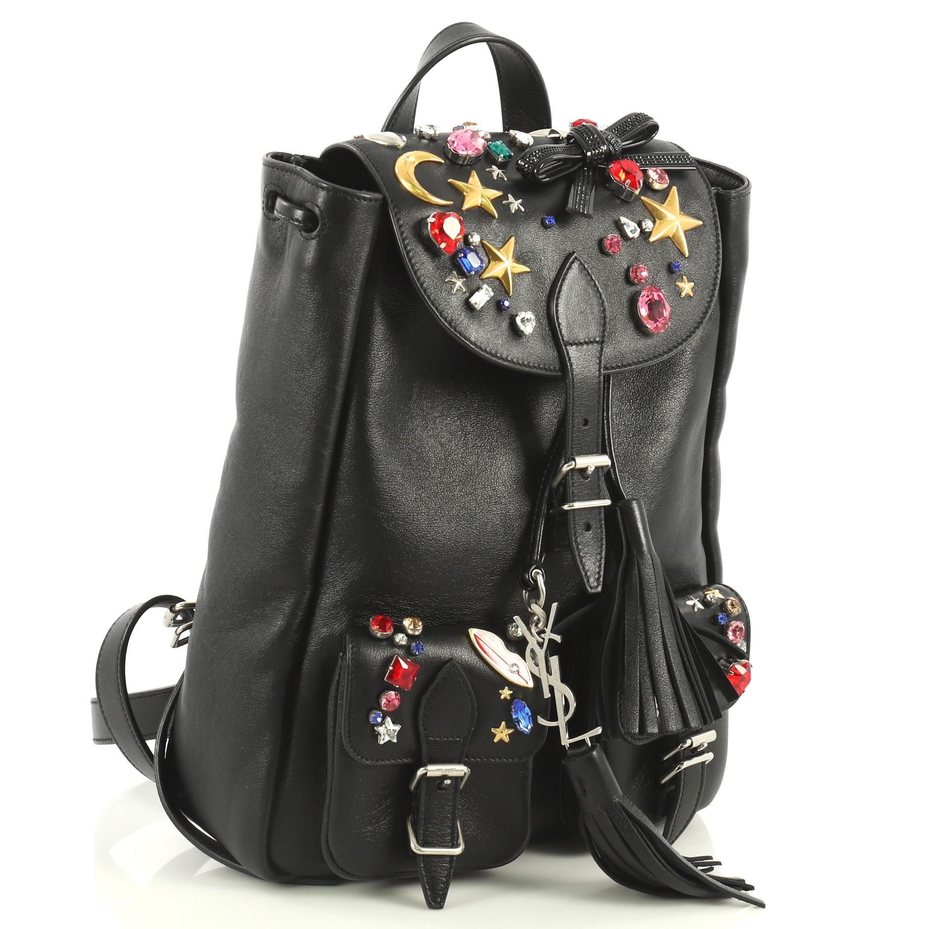 This Saint Laurent Festival Backpack Embellished Leather Small, crafted from black leather, features adjustable leather shoulder straps, gemstone embellishments, two exterior front pockets with buckles, top flap with buckle closure, and silver-tone