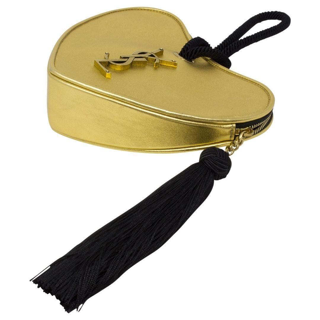 Ridiculously fabulous! This stylish minaudière is crafted of metallic gold calfskin leather in the shape of a heart. The handbag features an aged gold YSL logo, a black rope wristlet handle, and a black tassel zipper pull. The top zipper opens to a