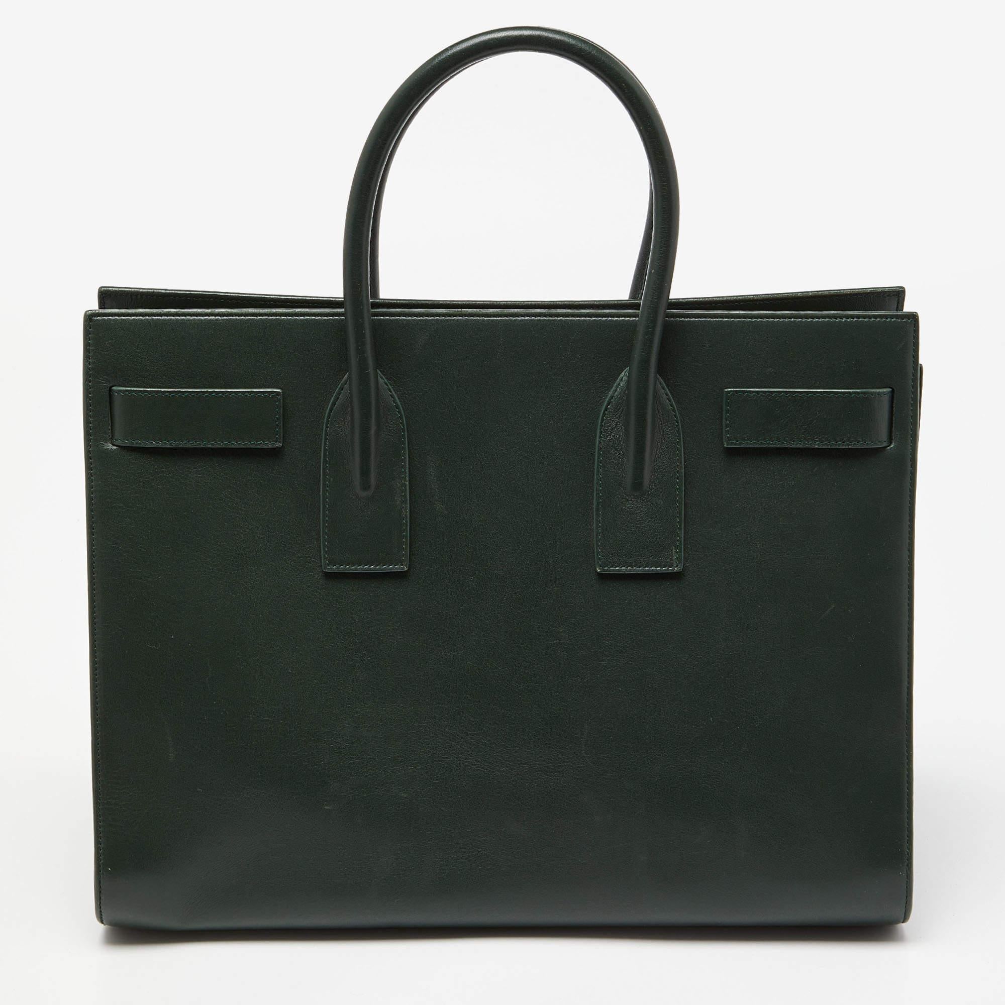 This Sac de Jour tote by Saint Laurent has a structure that exhibits a sophisticated image. Crafted from green leather, the bag can be carried in a chic way by double top handles and a shoulder strap. The tote comes with a stylish interior with