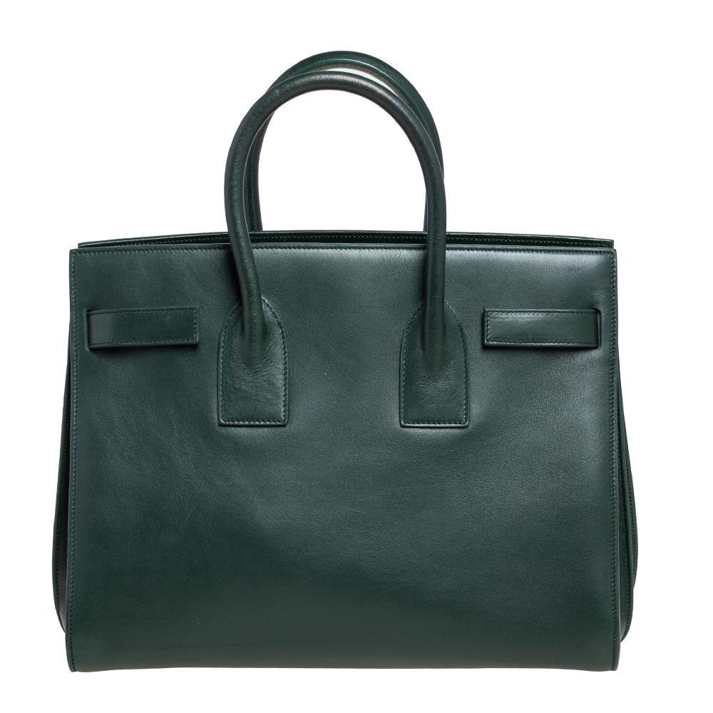 This Sac de Jour tote by Saint Laurent has a structure that simply spells sophistication. Crafted from green leather, the bag is held by double top handles. The tote comes with a suede-lined interior with enough space to store your necessities and