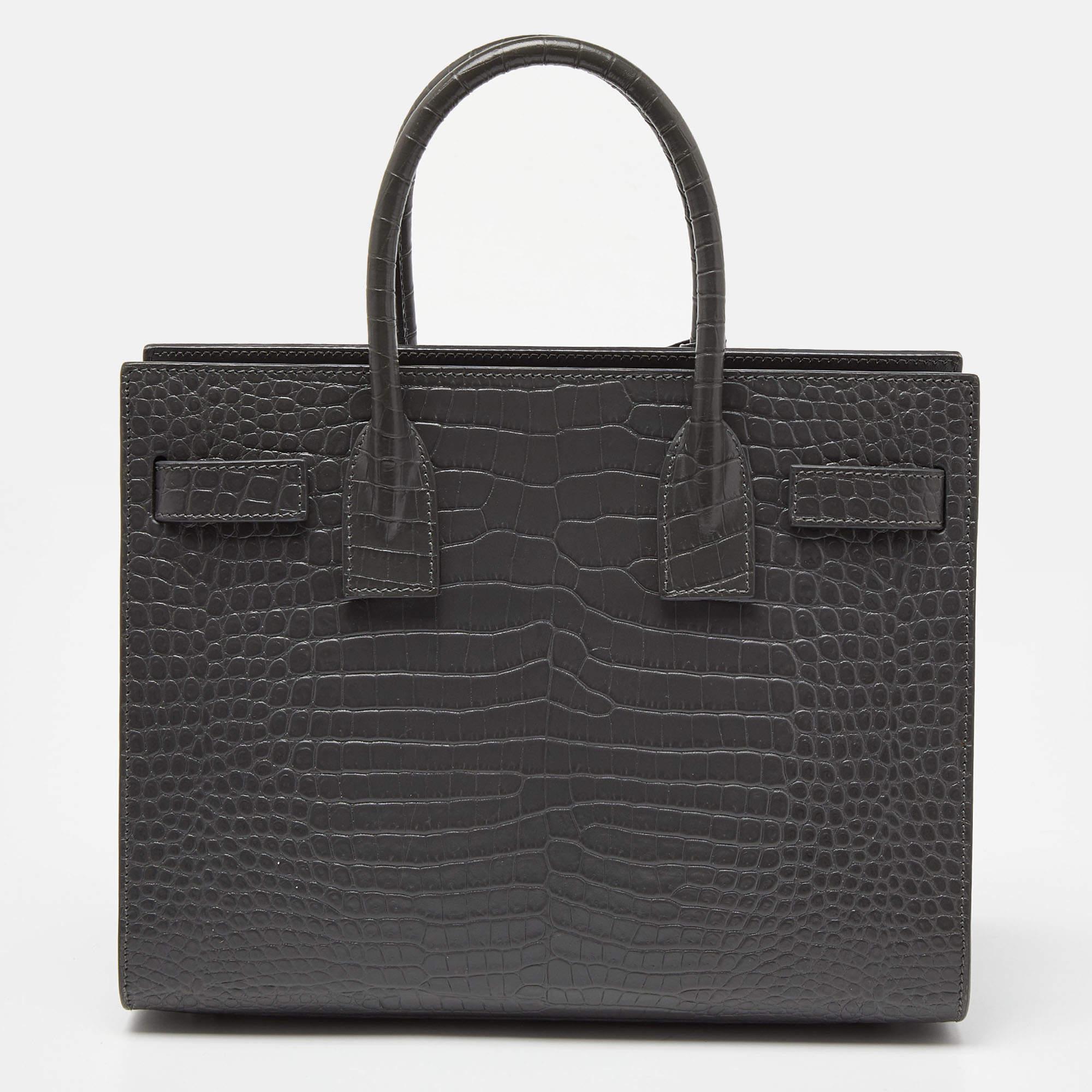 This Baby Classic Sac de Jour tote by Saint Laurent is a beauty. Crafted from grey croc-embossed leather, the bag is held by double top handles and a shoulder strap. The tote comes with a leather-lined interior with enough space to store your