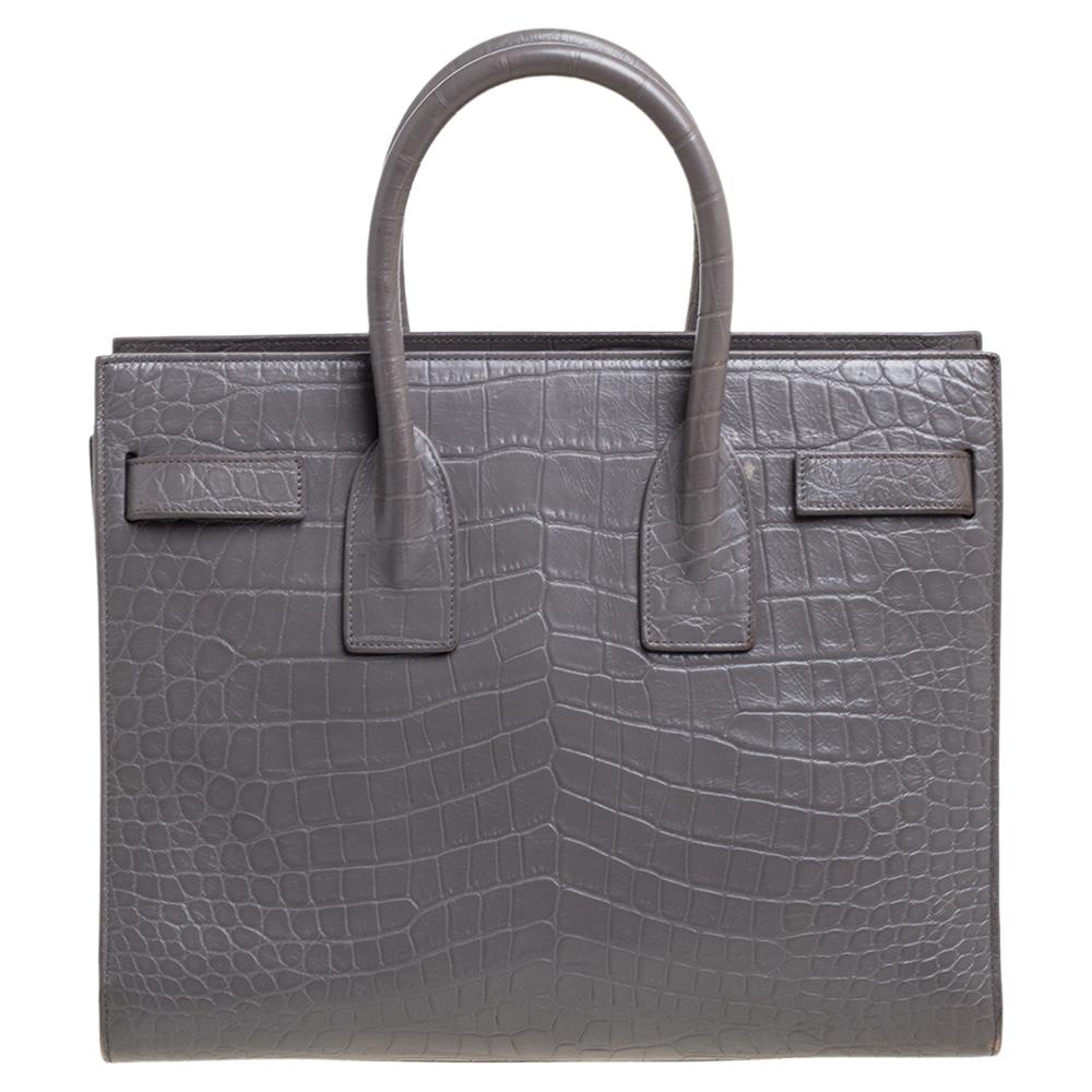 This Sac de Jour tote by Saint Laurent has a structure that simply spells sophistication. Crafted from grey croc-embossed leather, the bag is held by double top handles. The tote comes with a leather and canvas-lined interior with enough space to