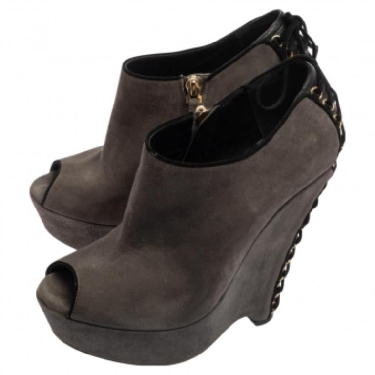 Flaunt perfection as you walk in these booties from the House of Saint Laurent. They are crafted using grey suede on the exterior. They feature peep-toe cuts, wedge heels, and zipper fastening. They are enhanced with gold-tone hardware. Make a