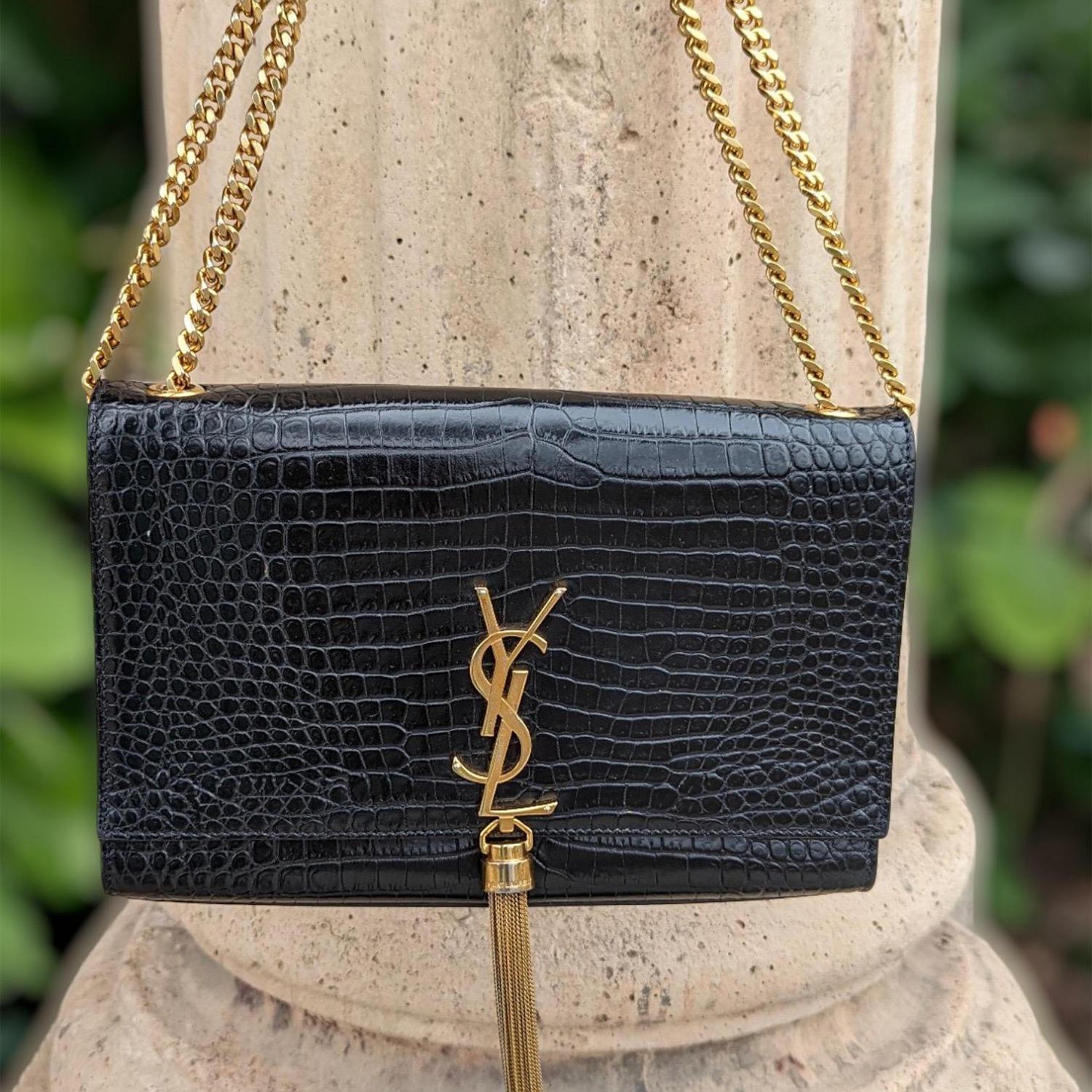 From the 2017 Collection by Anthony Vaccarello; Saint Laurent Kate Tassel Shoulder Bag. Crafted from croc-embossed leather in black. The bag features a gold chain link shoulder strap, a detailed tassel flap that opens to a black interior with a