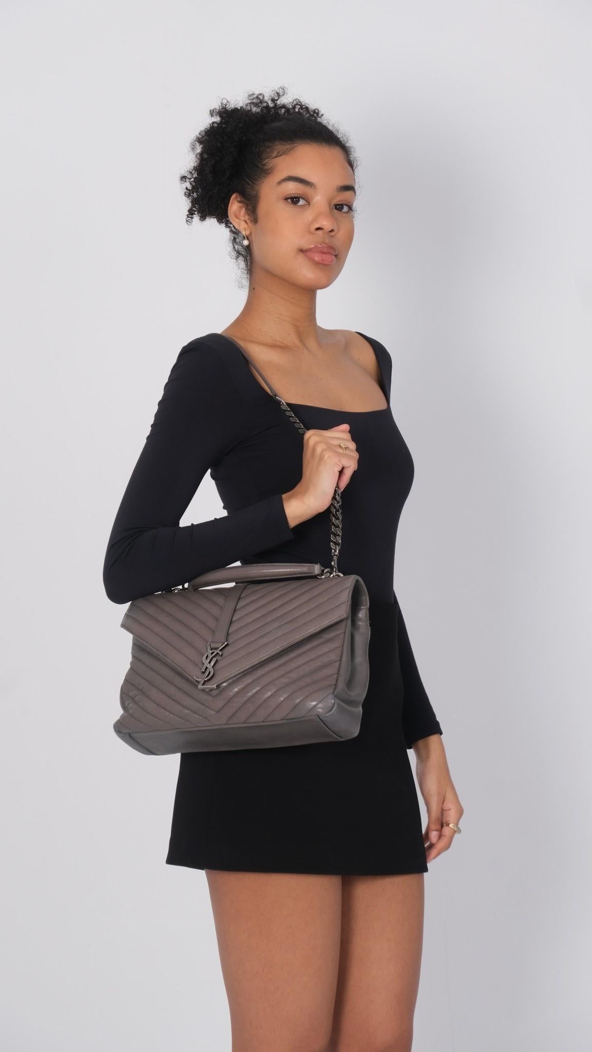 This shoulder bag is made of chevron-quilted leather in black. The bag features a rear patch pocket, an optional aged ruthenium bijoux chain-link shoulder strap with a shoulder pad, a leather top handle, and a front flap with a prominent aged