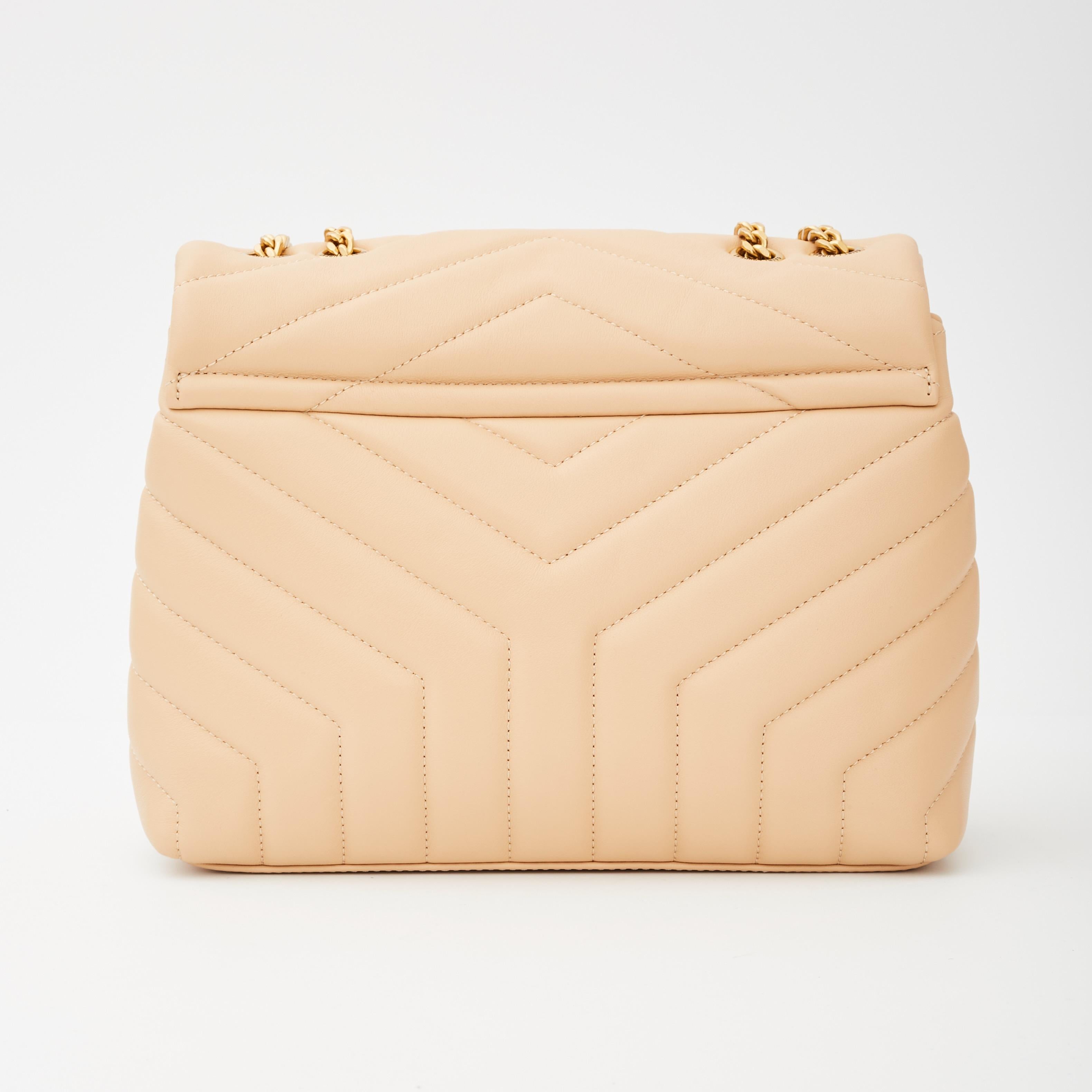 This shoulder bag features chevron quilting at both the front and the back with smooth calfskin leather in beige. The bag features a gold chain link shoulder strap with matching leather shoulder pads. The frontal flap features a prominent gold tone