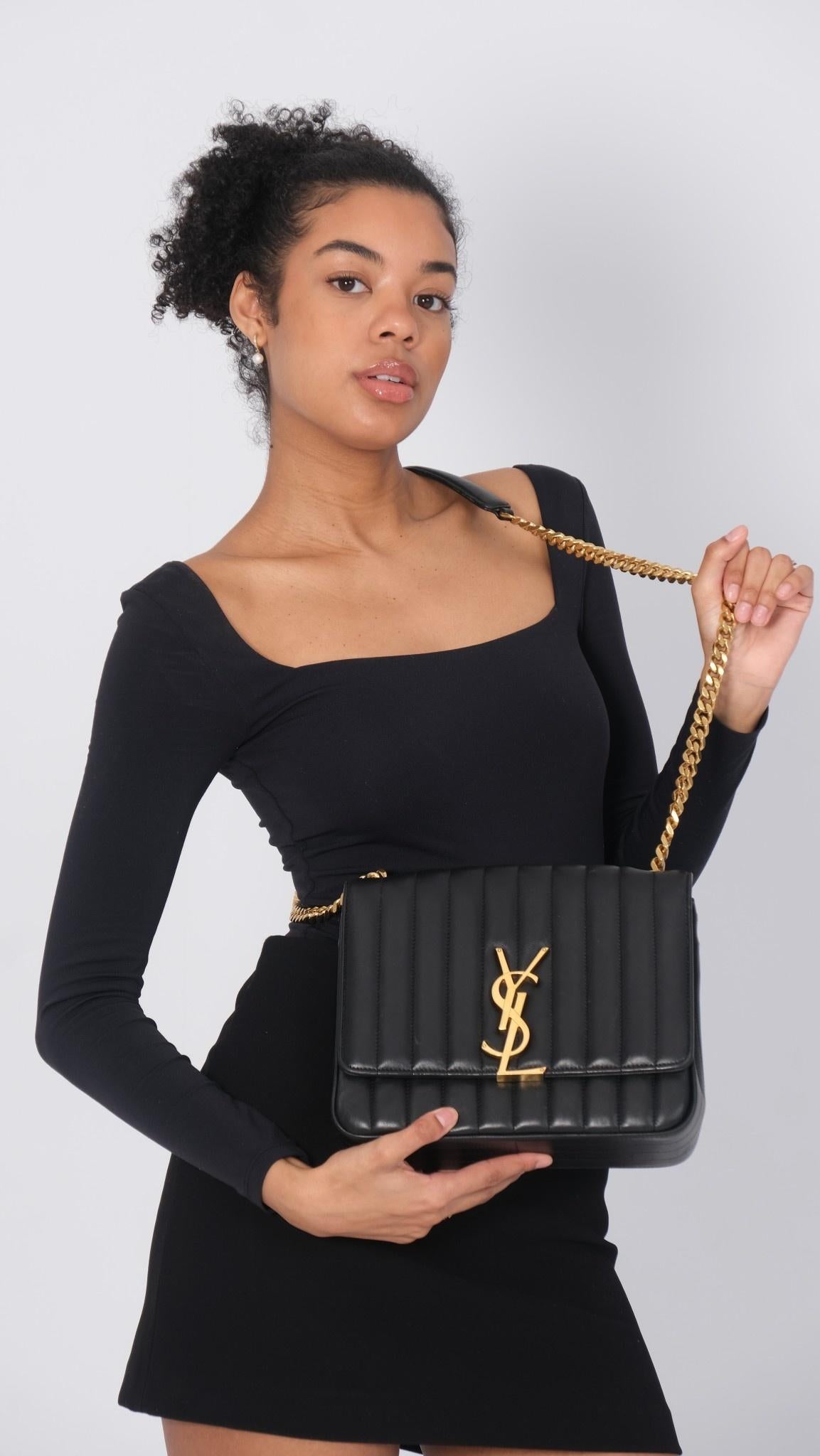 This shoulder bag is made of black lambskin quilted leather. The bag features a gold chain link shoulder strap with a matching leather shoulder pad. The frontal flap features a prominent gold YSL monogram detail and opens to a black leather interior