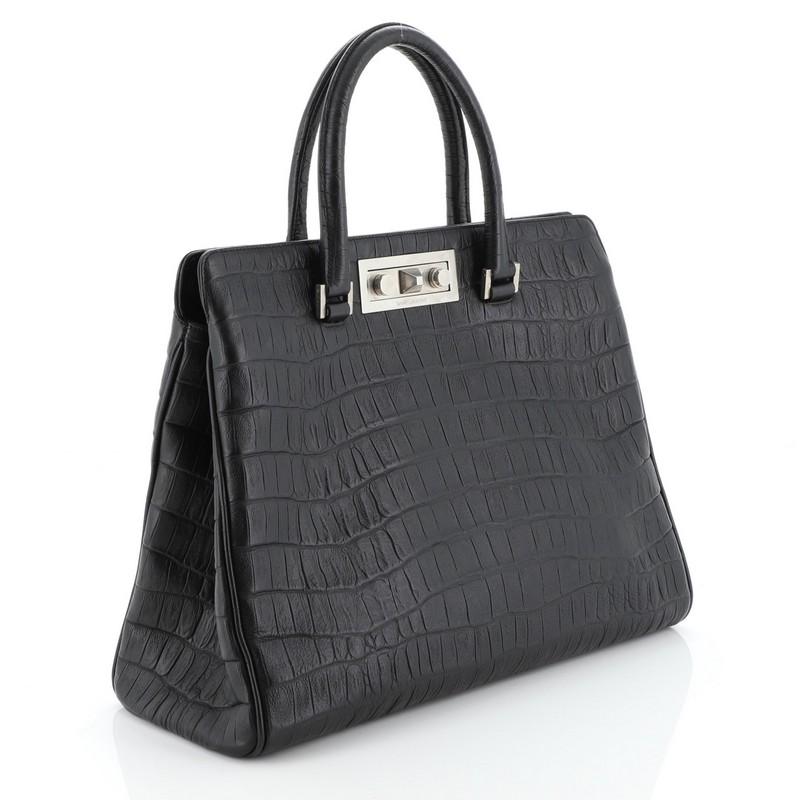 Este bolso Saint Laurent Manhattan Tote Pequeño de piel con relieve de cocodrilo, confeccionado en piel negra, tiene dos asas planas y herrajes en tono plateado envejecido. Su cierre se abre a un interior de ante negro. 

Precio de venta estimado: