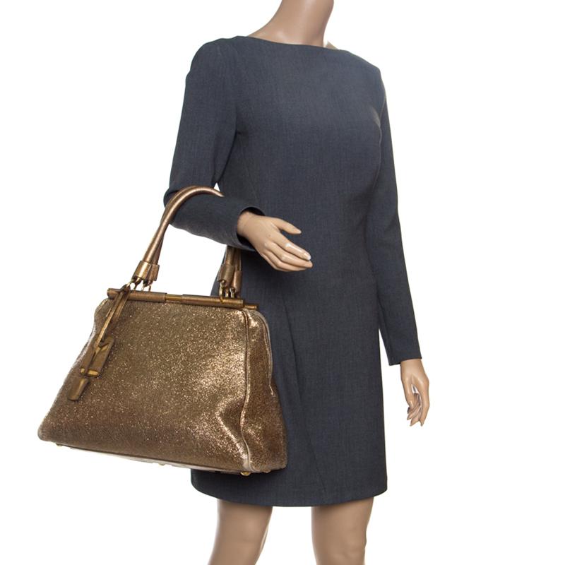This luxe Majorelle tote by Yves Saint Laurent is gorgeous! Crafted in golden metallic leather, It will carry your everyday essentials in style. The bag has a sleek structured design with two metal frame rods. It features a YSL luggage tag, lock,