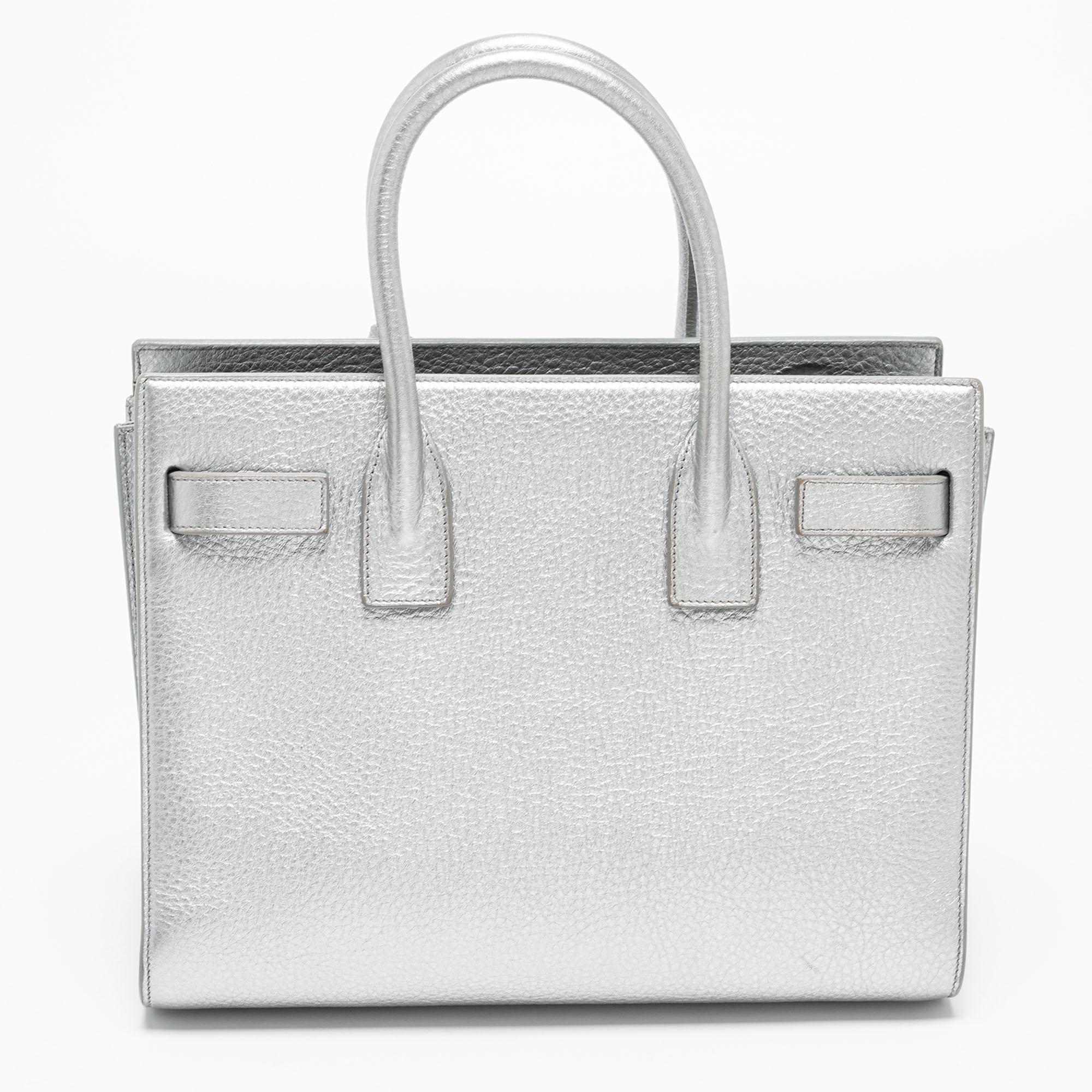 From Saint Laurent, this Baby Classic Sac De Jour tote is designed to offer complete essentiality, luxury, and style. Its structured silhouette is made from and accentuated with dual handles and silver-toned hardware. It accommodates a leather-lined