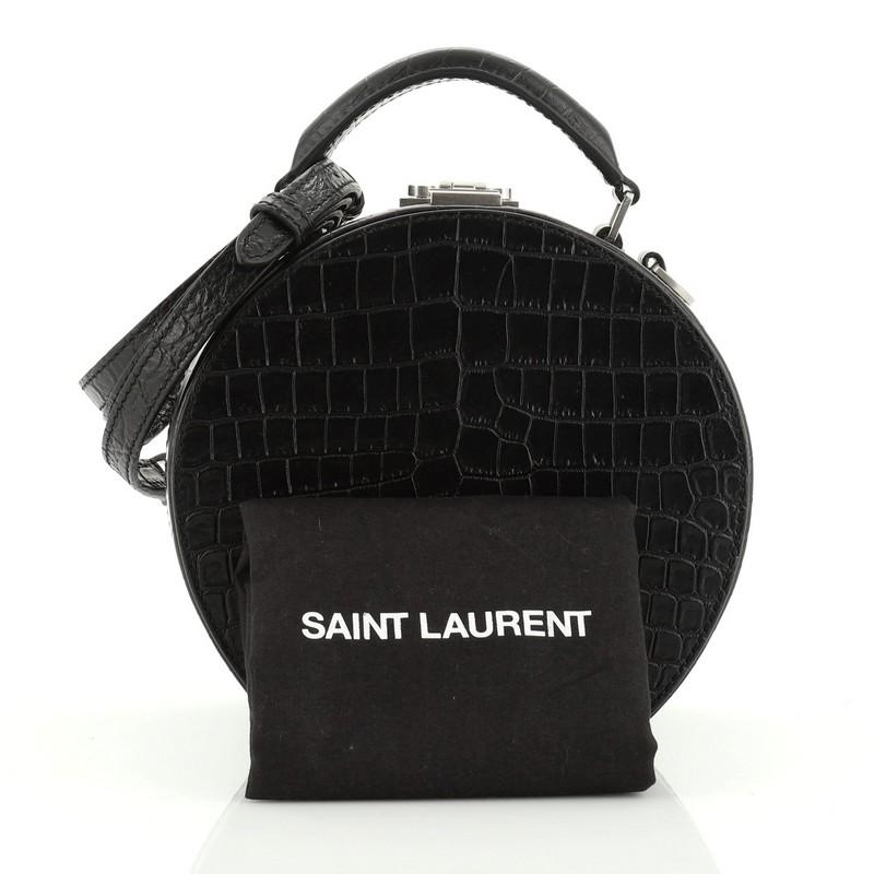 This Saint Laurent Mica Hatbox Bag Crocodile Embossed Leather Small, crafted in black crocodile embossed leather, features an adjustable leather handle, leather top handle. Its buckle closure opens to a black fabric interior with slip pocket.