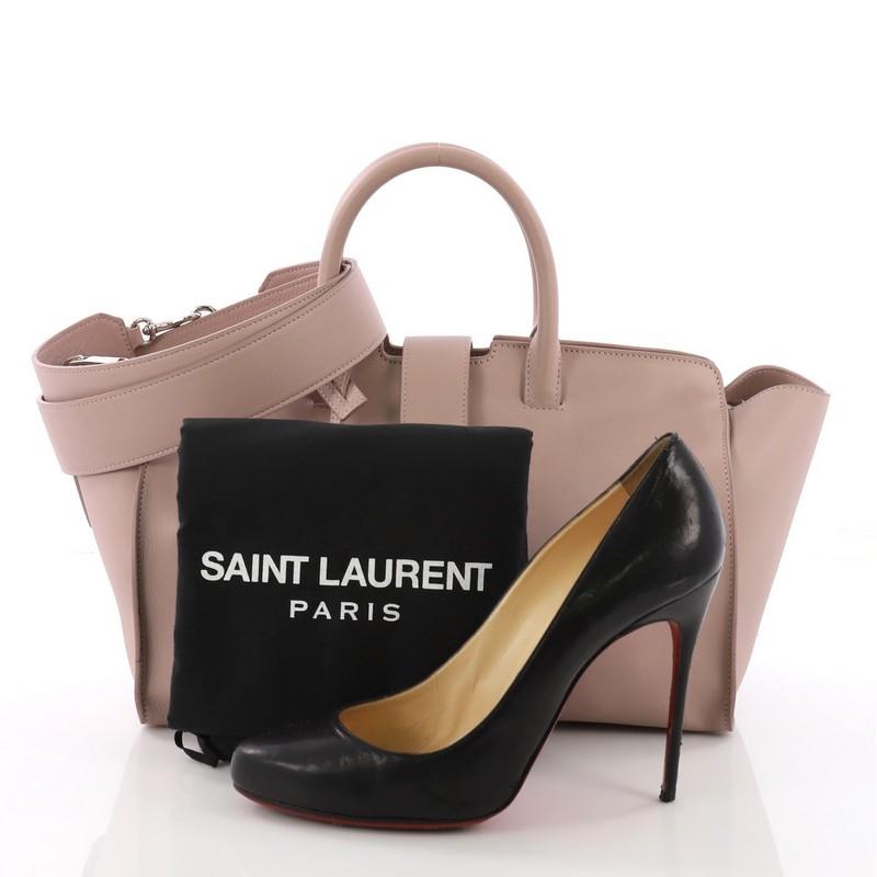 This Saint Laurent Monogram Cabas Downtown Leather Small, crafted in pale pink leather, features dual rolled handles, YSL metal logo at the front, and silver hardware. Its magnetic snap and zip closure opens to a pale pink suede interior with slip
