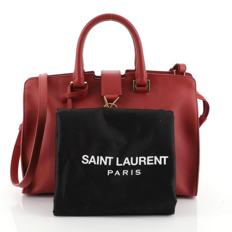 This Saint Laurent Monogram Cabas Leather Baby, crafted from red leather, features dual rolled leather handles, classic 'YSL' monogram flap hardware piece, protective base studs, and gold-tone hardware. Its zip closure opens to a red raw leather and