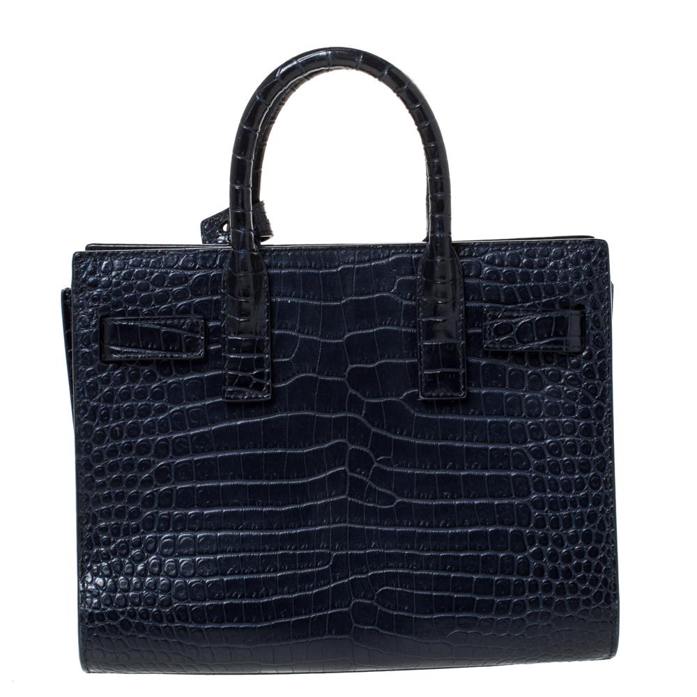 This Sac de Jour tote bag by Saint Laurent Paris has a sophisticated look. Crafted from croc-embossed leather, the bag has dual round handles and protective metal feet. The tote comes with a leather-lined interior that has enough space to store your