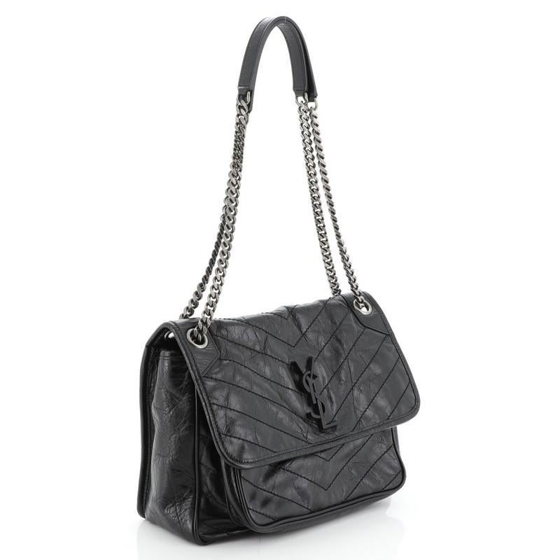 This Saint Laurent Niki Chain Flap Bag Matelasse Chevron Leather Medium, crafted in black matelasse chevron leather, features chain link shoulder straps with leather pads, frontal flap with YSL monogram detail, and aged silver-tone hardware. Its