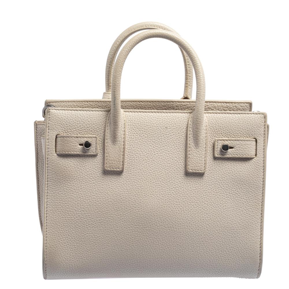 This Sac de Jour tote by Saint Laurent has a structure that simply spells sophistication. Crafted from off-white leather, the bag is held by double top handles. The tote comes with a suede-lined interior with enough space to store your necessities