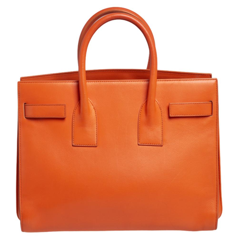 This Sac de Jour tote by Saint Laurent has a structure that simply spells sophistication. Crafted from orange leather, the bag is held by double top handles. The tote comes with a suede-lined interior with enough space to store your necessities and