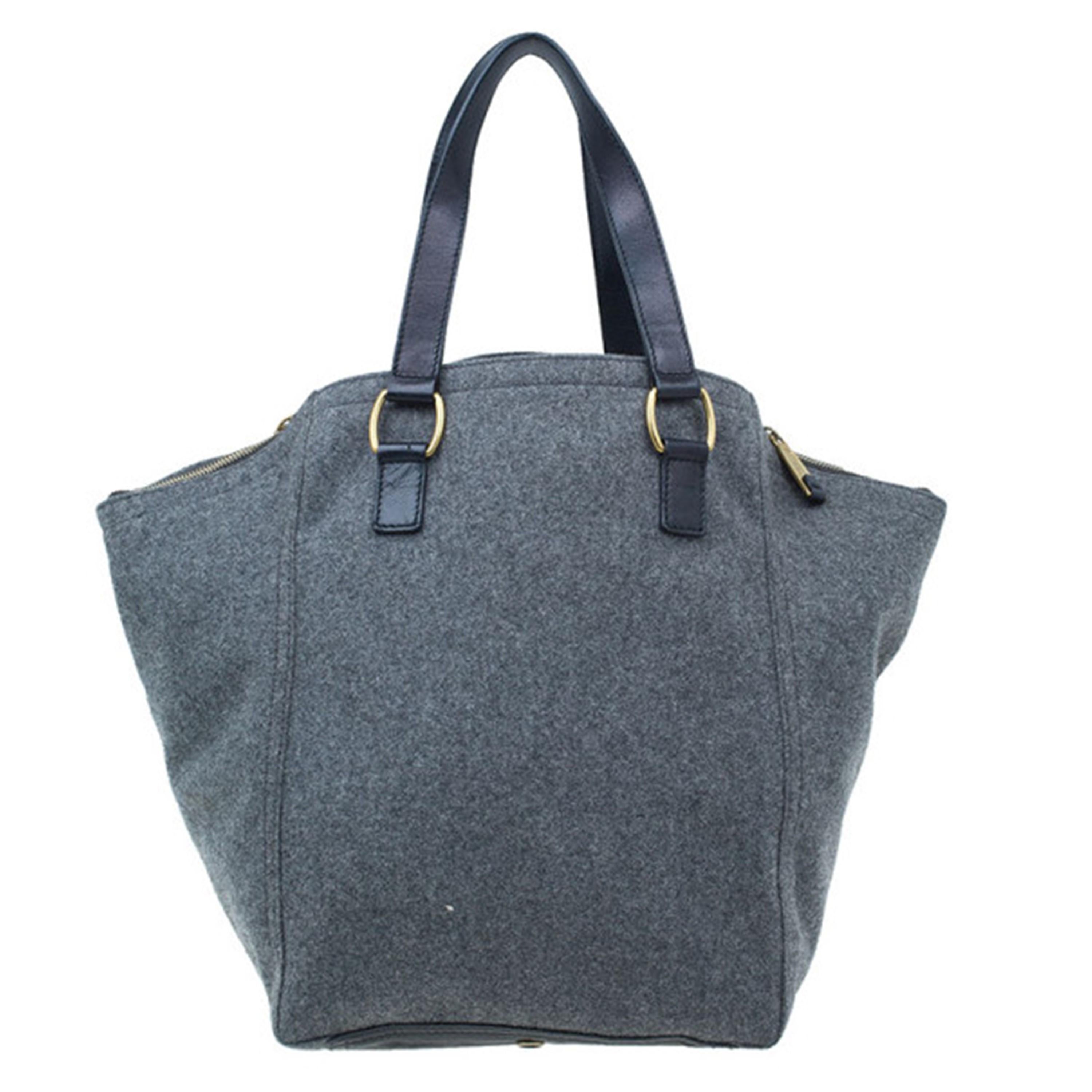 Make a statement with this big yet bold Saint Laurent Paris Downtown tote. Made from light grey felt, this stylish handbag is accent with brown leather, a front pocket with zippers, as well as gold tone studs and buckles. The spacious interior