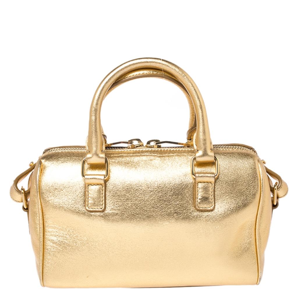 This stylish duffel bag comes from the house of Saint Laurent Paris. It has been crafted in Italy and made from quality leather. It flaunts a metallic gold hue that adds a touch of glamour. It is styled with dual handles, a shoulder strap, double