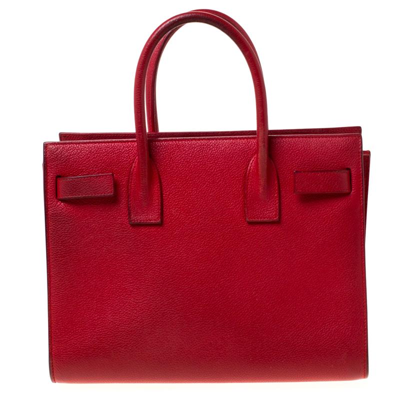 This Sac de Jour tote by Saint Laurent has a structure that simply spells sophistication. Crafted from red leather, the bag is held by double top handles and a shoulder strap. The tote comes with a fabric-lined interior with enough space to store