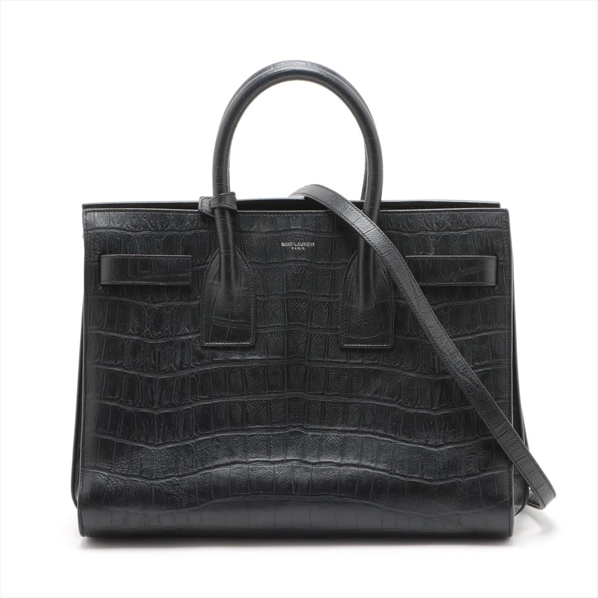 The Saint Laurent Paris Sac de Jour Croc Two-Way Handbag in Black is a luxurious and versatile accessory that exudes timeless sophistication. Crafted from exquisite croc-embossed leather, the handbag boasts a structured silhouette with clean lines