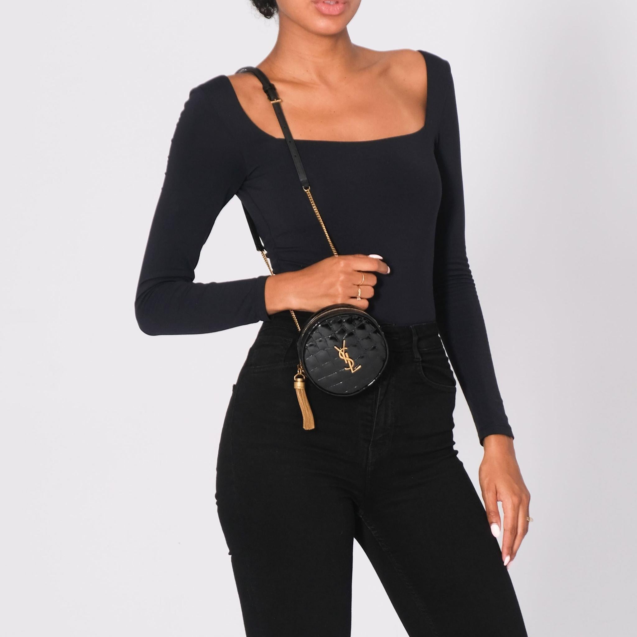 Diese runde Crossbody ist aus Lackleder mit Krokoprägung gefertigt. Die Tasche verfügt über einen Schulterriemen mit goldenen Kettengliedern, einen passenden Reißverschluss an der Oberseite und ein sichtbares YSL Monogramm. Der Reißverschluss führt