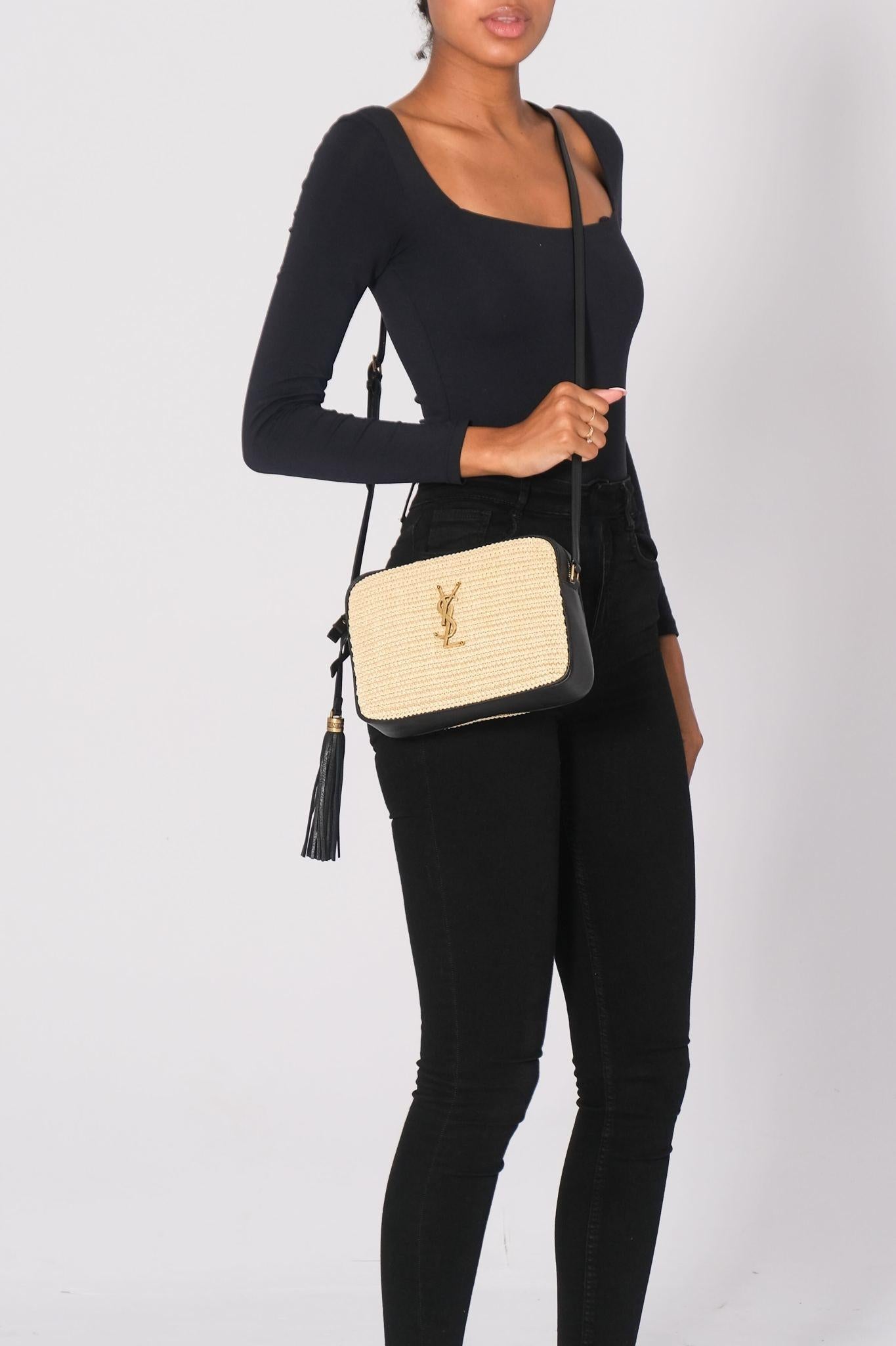 This shoulder bag is made of raffia in beige with black leather trim and details. The bag features an adjustable crossbody strap and brass hardware. The top zipper opens to a compact black fabric interior with a pocket. Retail.

Color: beige with
