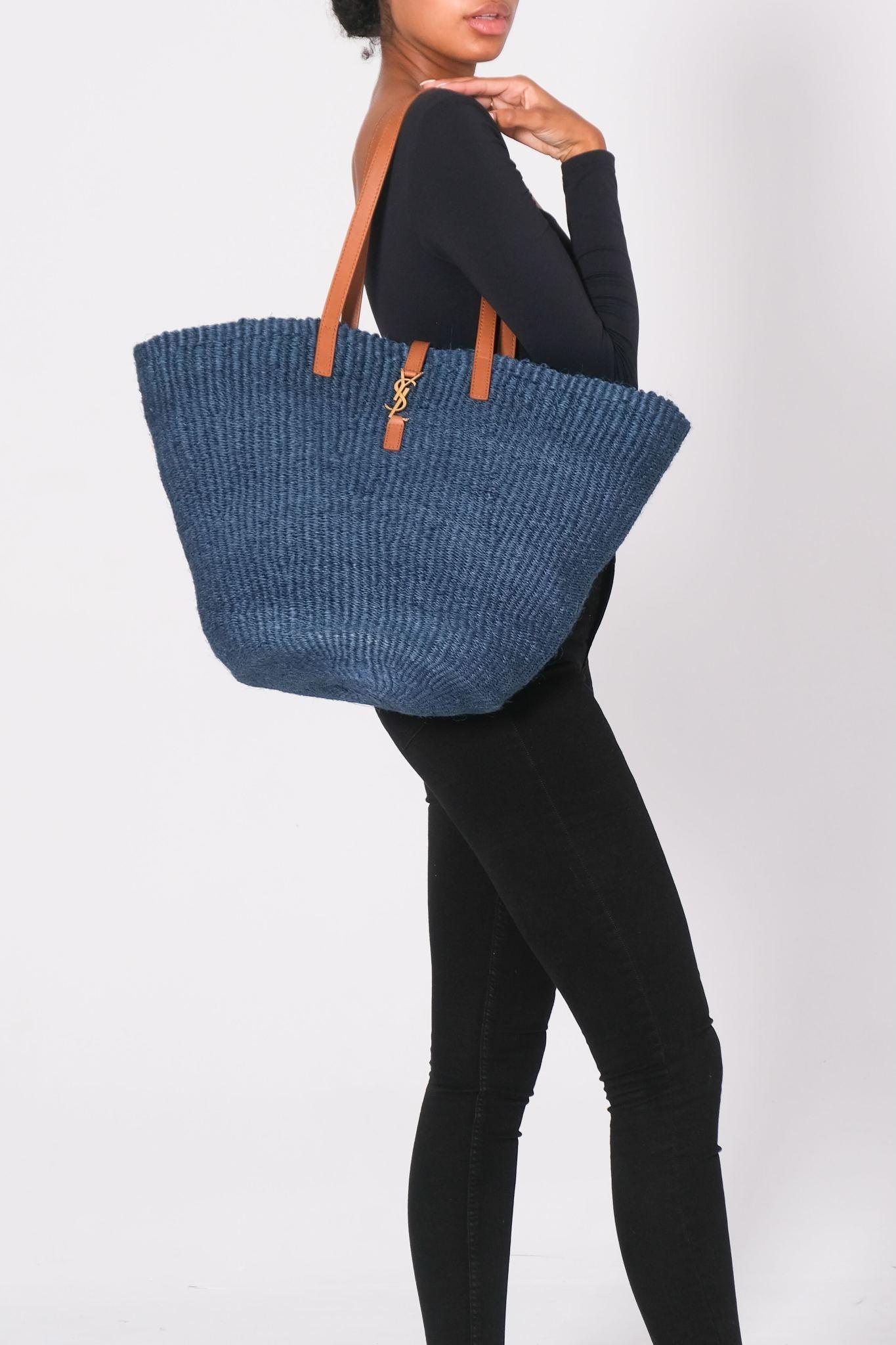 This tote is made of blue woven straw, with brown leather handles. The top is open to a spacious matching woven straw interior. Outlet.

Color: blue
Material: raffia
Model No. 688221
Comes with: dust bag
Condition: Excellent.
Made in