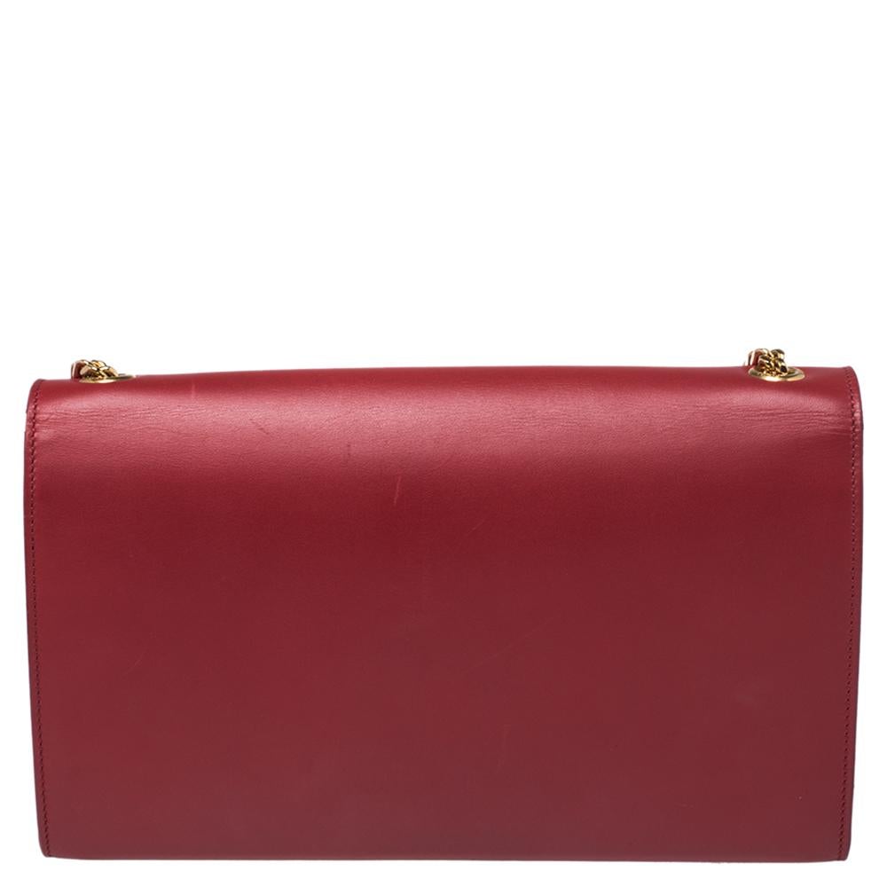 Ravishing in red, this Kate Saint Laurent bag is sure to lend you a glamorous look. It has been crafted from leather and styled with a gold-tone 'YSL' logo and a tassel on the front flap. It opens to a fabric-lined interior and has a shoulder