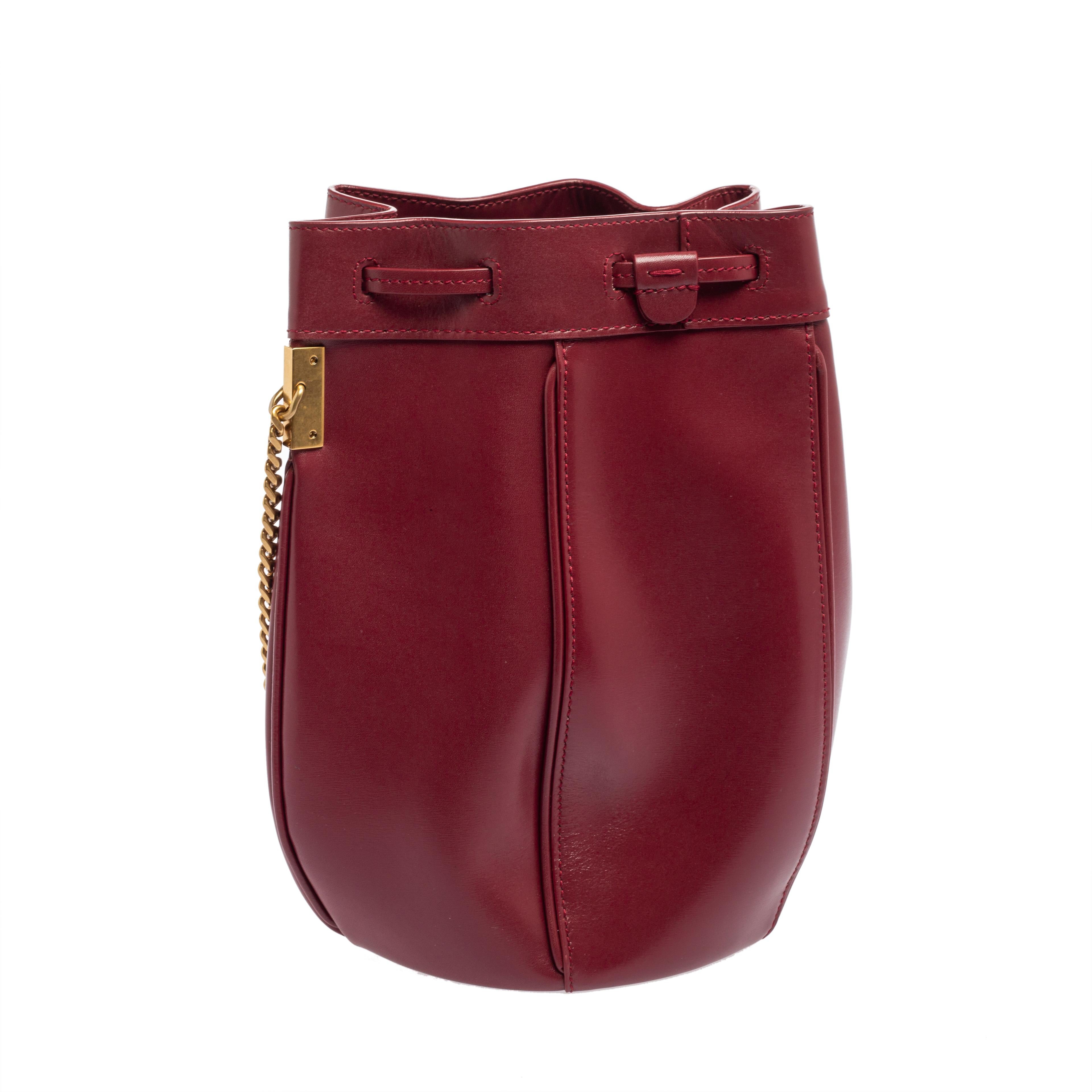 Minimal and chic are some words that describe this Saint Laurent bucket bag! Crafted from red leather, the creation is added with a well-spaced interior, drawstring closure, signature stamp at the front, and a shoulder chain that can be worn across
