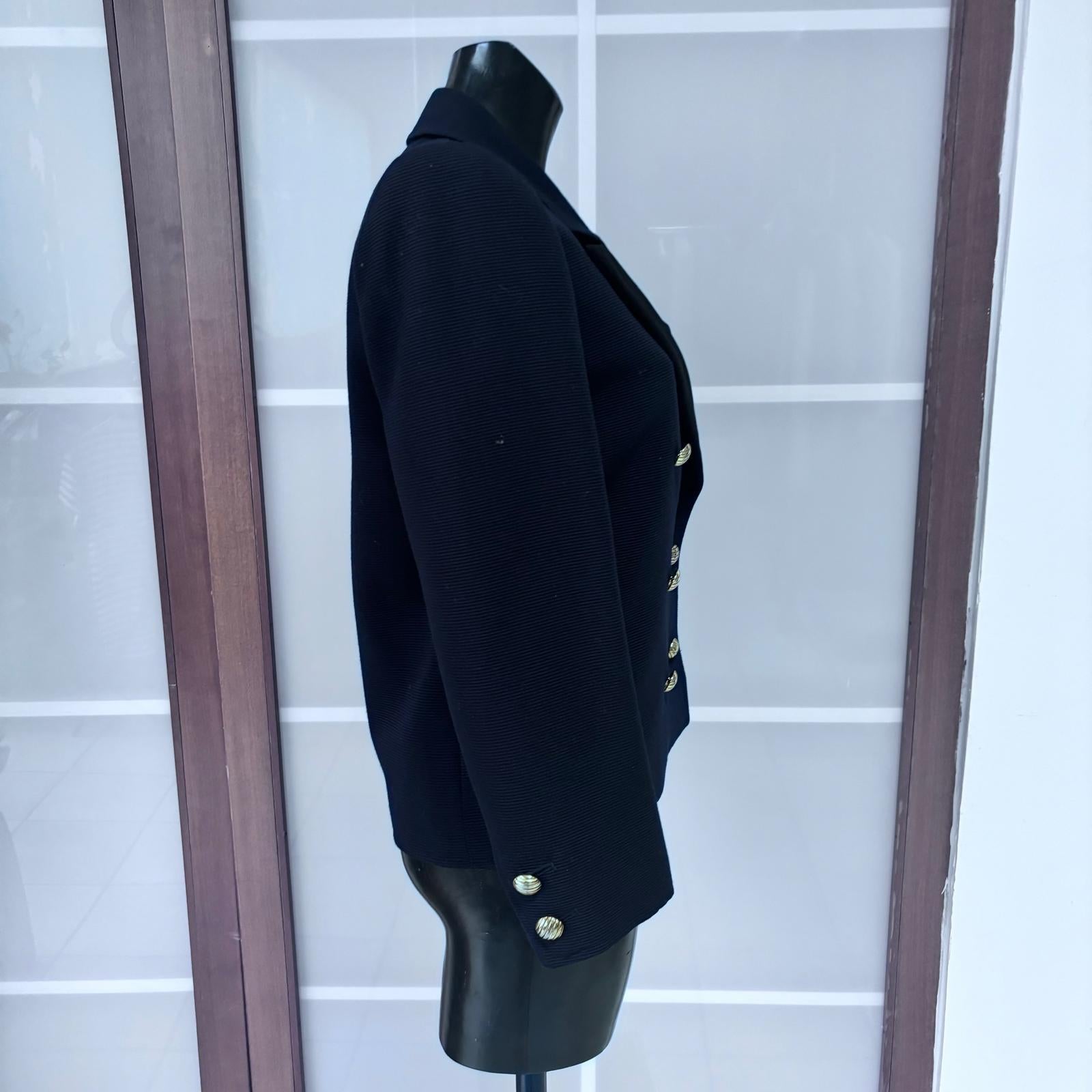 Élégant et intemporel, ce blazer Saint Laurent Rive Gauche des années 1980 incarne le style emblématique de la maison française. Confectionné en laine bleu marine à la texture compacte, il est agrémenté de revers en satin noir et d'une fermeture à