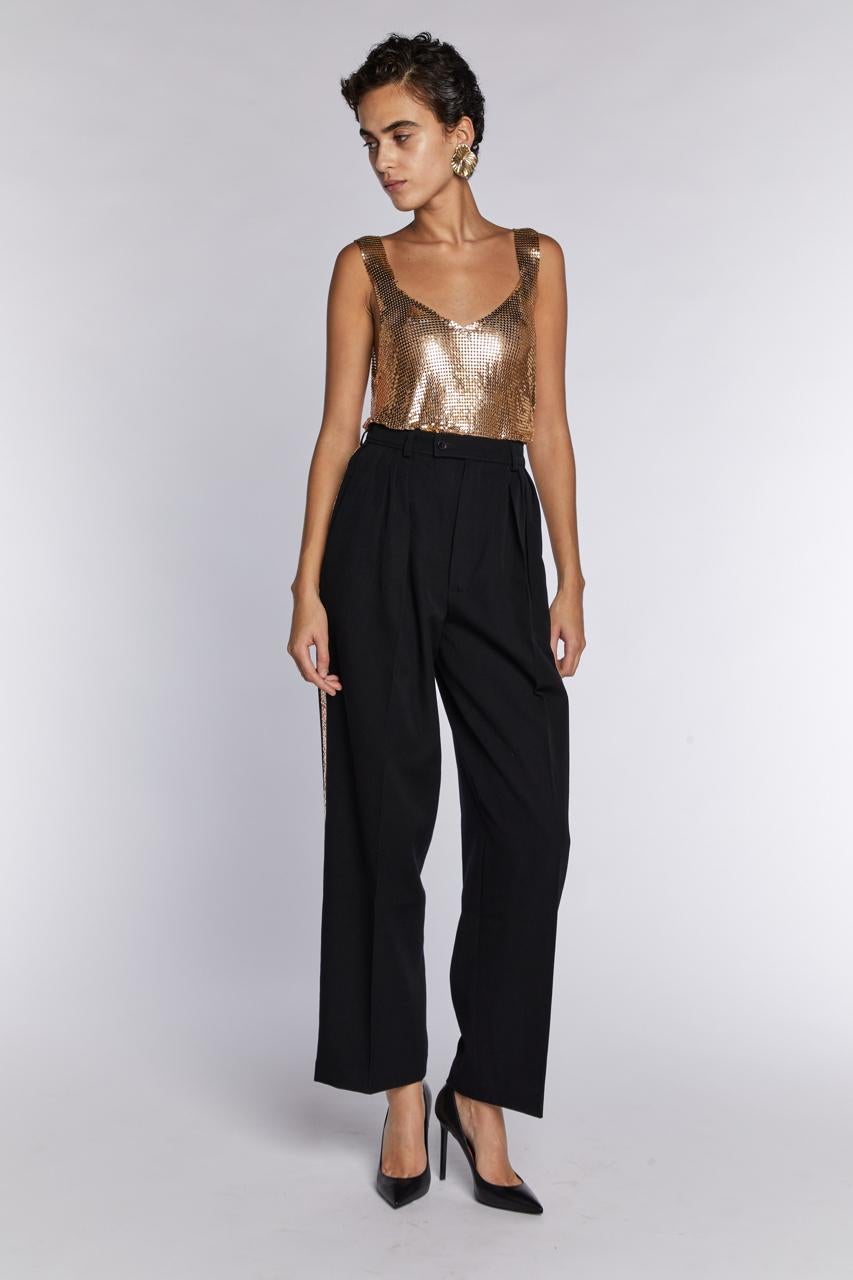 - Saint Laurent Rive Gauche Cira 1985 de Yves Saint Laurent

- Vendido por Mae Vintage London 

- Pantalón de lana de talle alto con raya esmoquin/ Le Smoking en lentejuelas doradas pálidas

- Peinado con un top Whitings and Davis disponible en