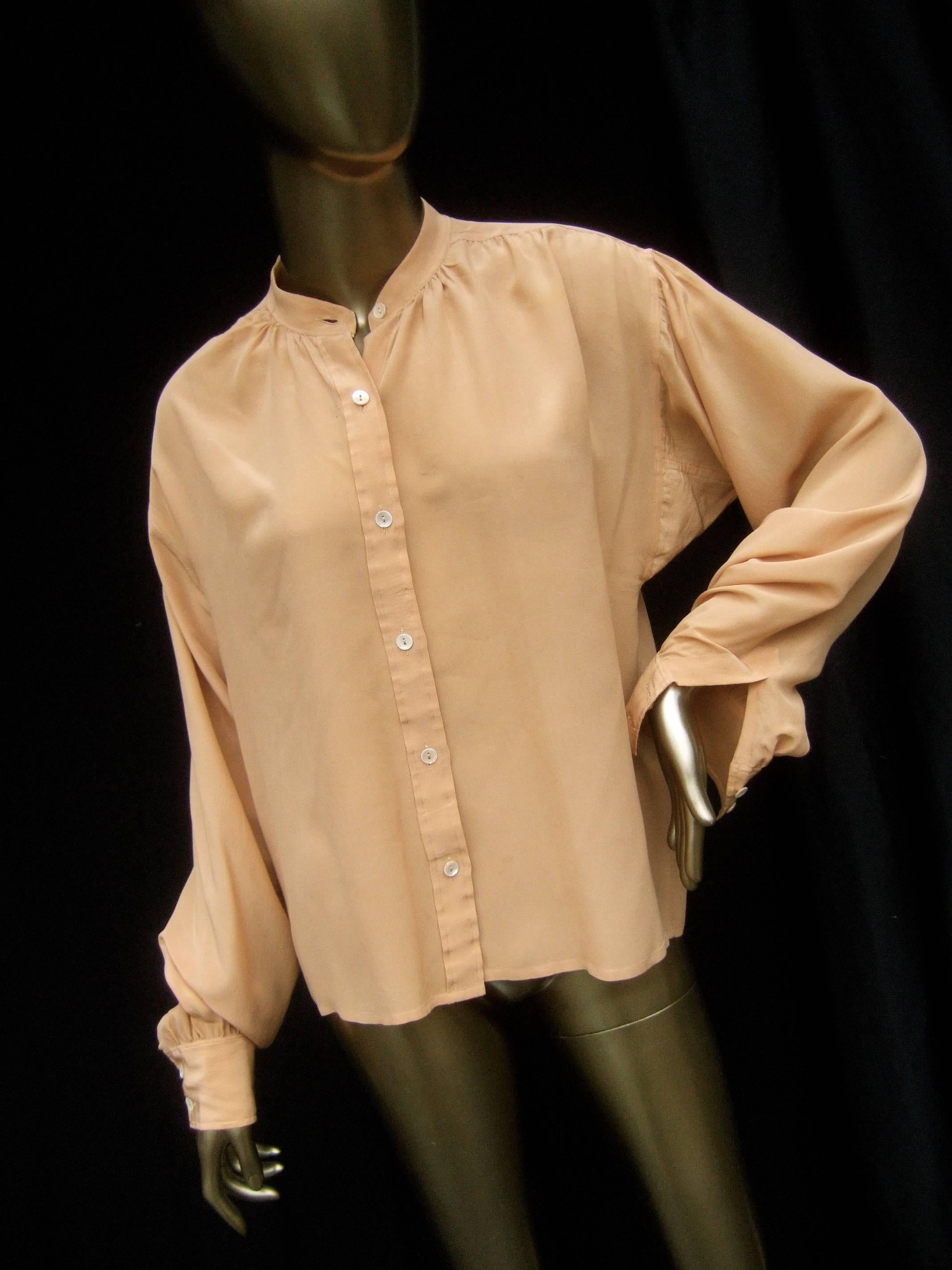 Saint Laurent Rive Gauche peach silk blouse c 1970s
The elegant peach color silk blouse is designed 
with a Nehru style stand up collar 

A series of tiny lucite buttons run down the front 
The sleeve cuffs have subtle pleated detail 
Makes an