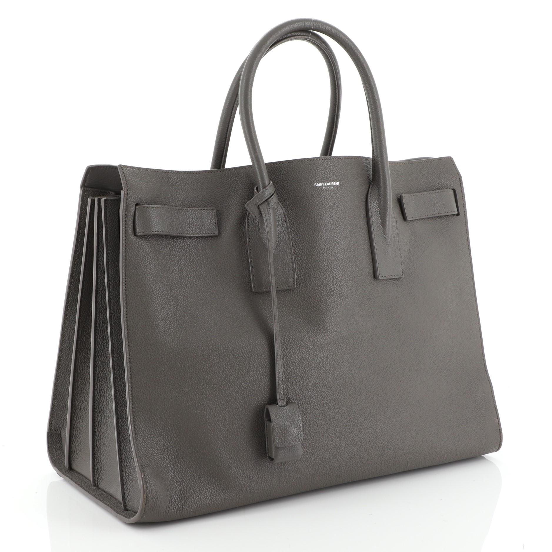 This Saint Laurent Sac de Jour Carryall NM Bag Leather Large, crafted from gray leather, features dual rolled leather handles, protective base studs, and silver-tone hardware. Its leather tabs open to a gray leather interior divided into two