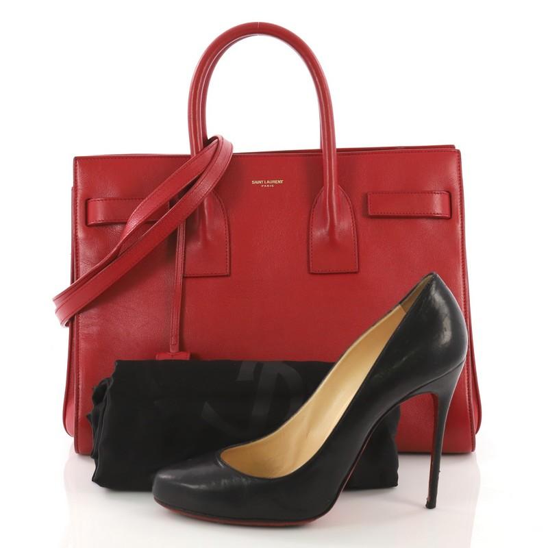 This Saint Laurent Sac de Jour Handbag Leather Small, crafted from red leather, features dual rolled leather handles, protective base studs, and gold-tone hardware. Its leather tabs open to a red suede interior divided into two compartments and a