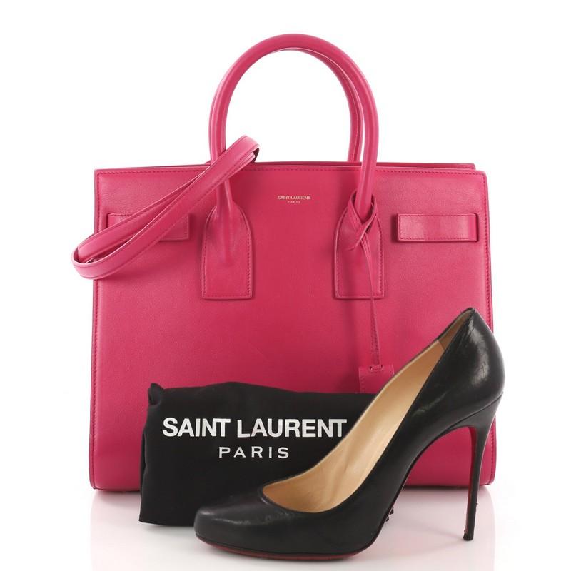 This Saint Laurent Sac de Jour Handbag Leather Small, crafted from pink leather, features dual rolled leather handles, protective base studs, and gold-tone hardware. Its leather tabs open to a pink suede interior divided into two compartments and a