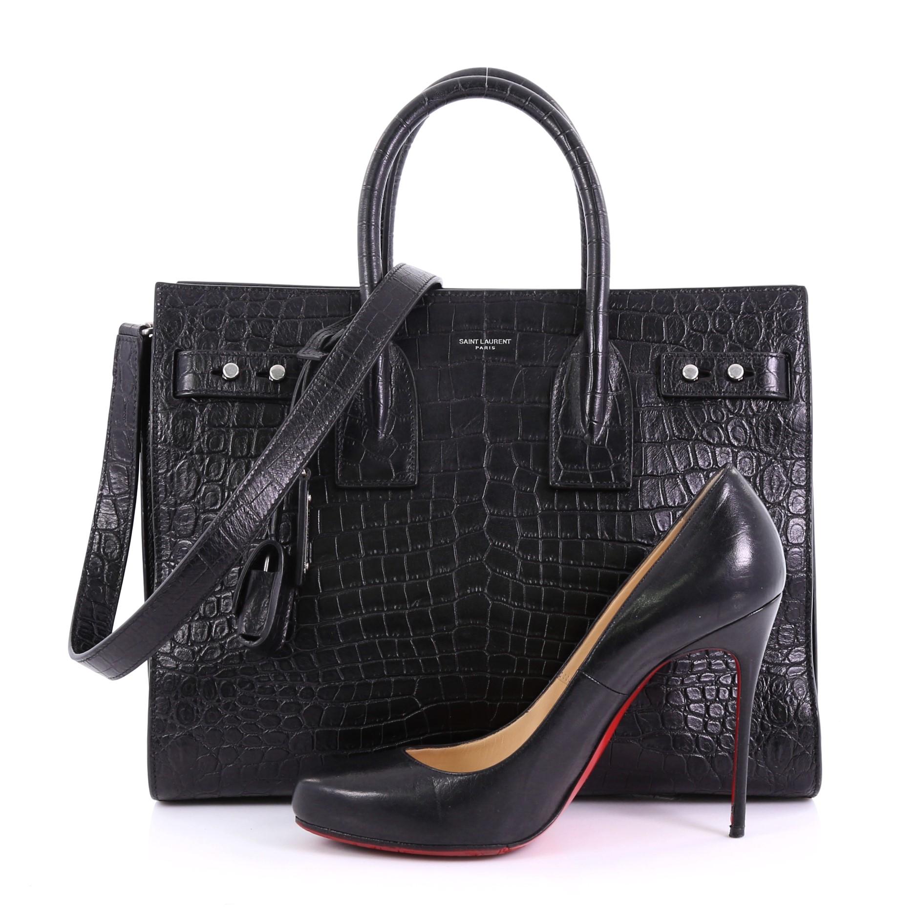 This Saint Laurent Sac de Jour Souple Bag Crocodile Embossed Leather Small, crafted from black crocodile embossed leather, features dual rolled leather handles, accordion sides, leather base feet, leather tabs threaded through side gussets, and