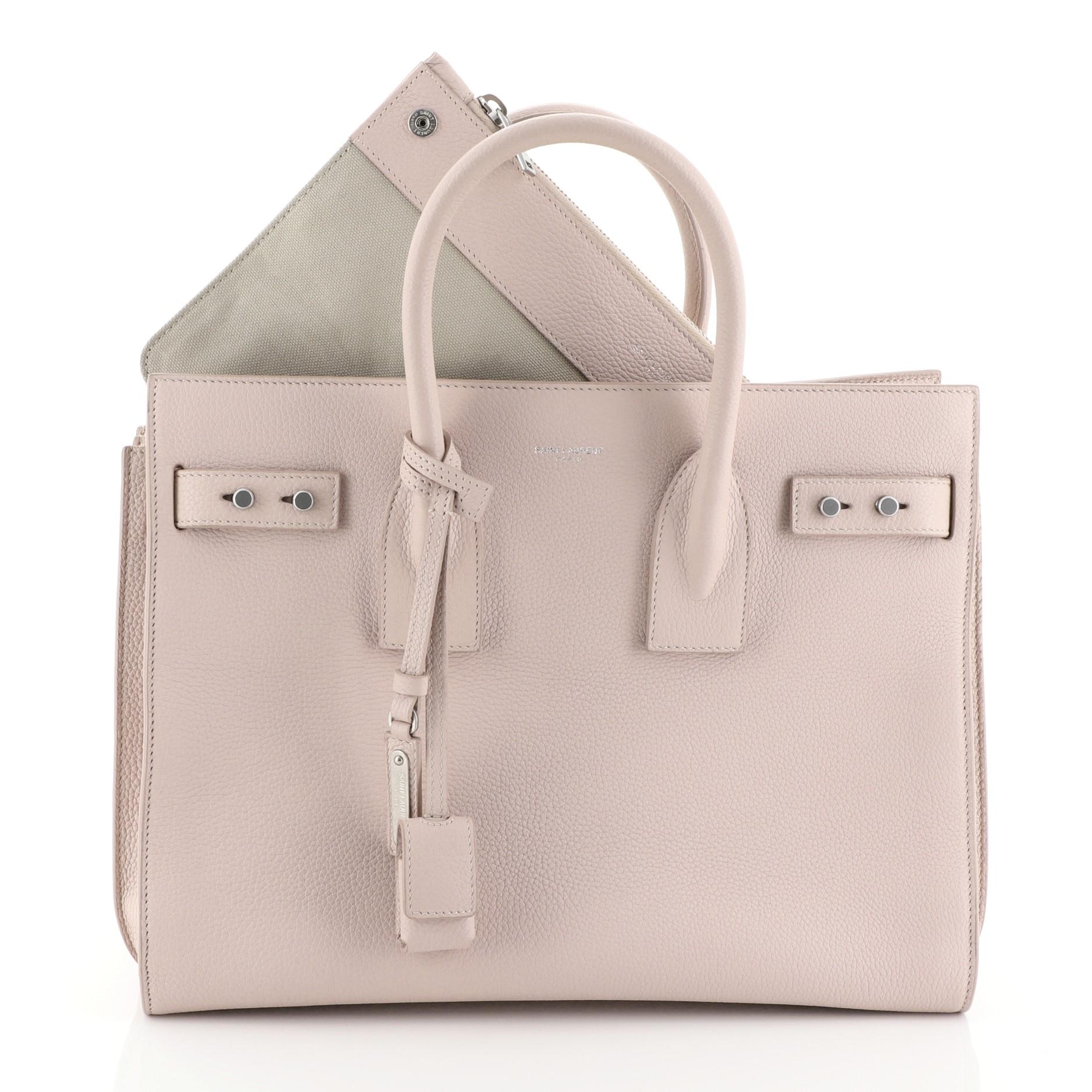 This Saint Laurent Sac de Jour Souple Bag Leather Small, crafted from pink leather, features dual rolled leather handles, accordion sides, leather tabs threaded through side gusset, and silver-tone hardware. It opens to a pink suede interior with