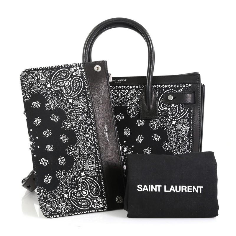 This Saint Laurent Sac de Jour Souple Bag Printed Canvas with Leather Baby, crafted in black leather and canvas, features dual-rolled leather handles, black and white bandana print and silver-tone hardware. It opens to a black leather interior