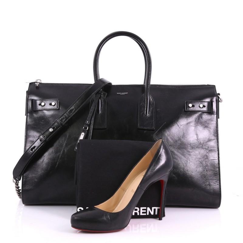 Ce Sac de Jour Saint Laurent Souple Duffle Bag Cracked Shiny Leather 36H:: réalisé en cuir noir craquelé brillant:: présente des poignées en cuir roulées:: des languettes en cuir enfilées dans les soufflets latéraux qui permettent au sac de se
