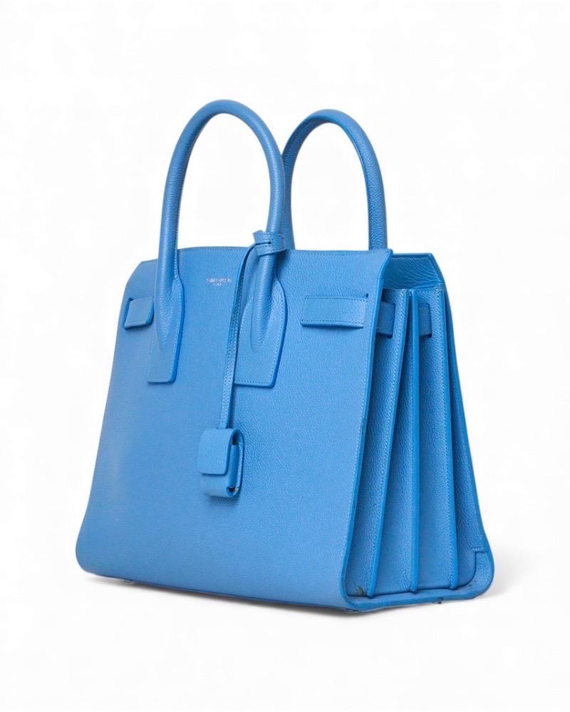 Borsa firmata Saint Laurent, modello Sac De Jours nella misura small, realizzata in pelle granulata azzurra con hardware argento. Non è dotata di nessuna chiusura, internamente rivestita in pelle liscia tono su tono con comoda tasca centrale. Muni