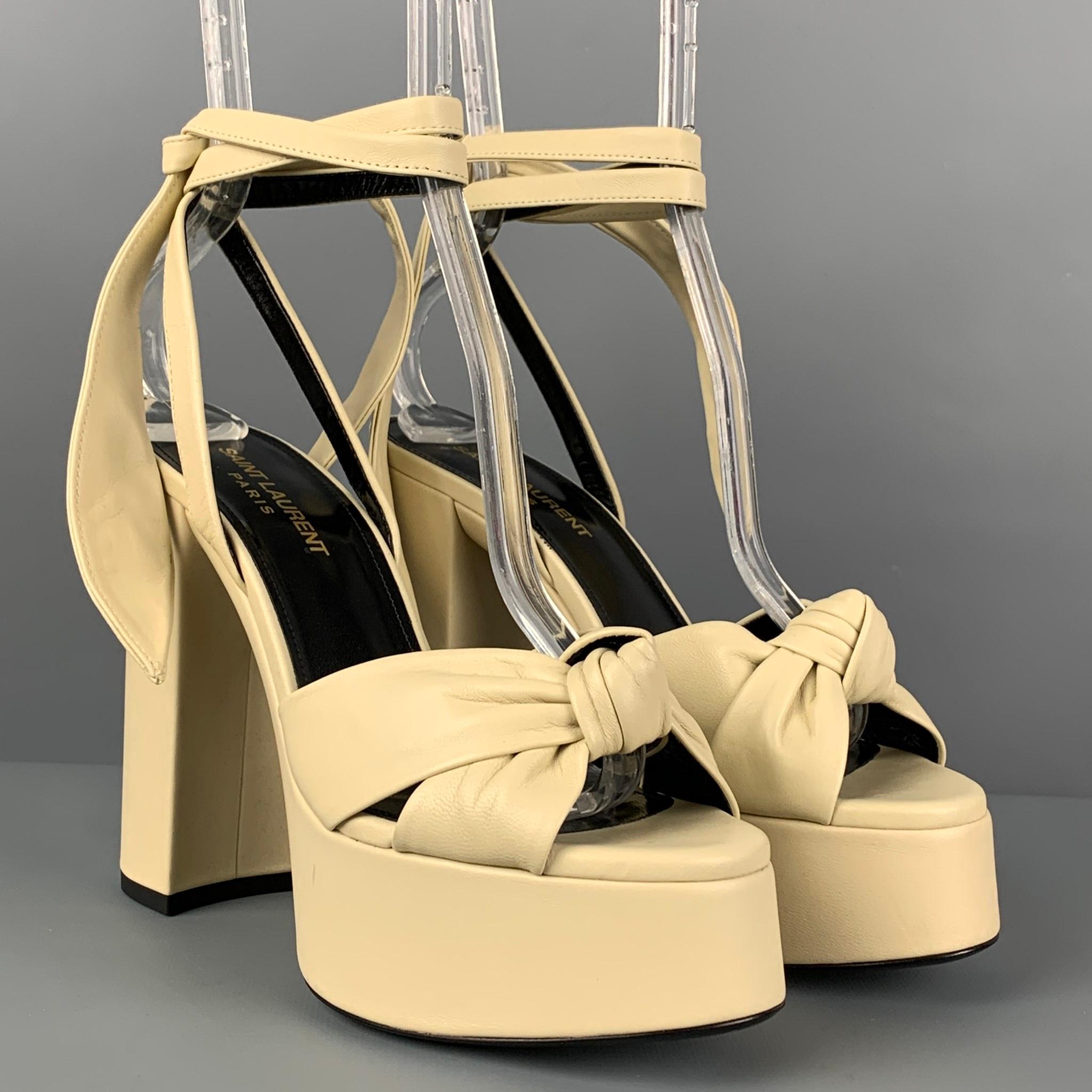SAINT LAURENT 'Bianca' sandals comes in a beige leather featuring a platform, ankle tie, front straps, and a chunky heel. Strap could be styled into a front bow. Made in Italy. 

Very Good Pre-Owned Condition. Light wear.
Marked: 37.5
Original